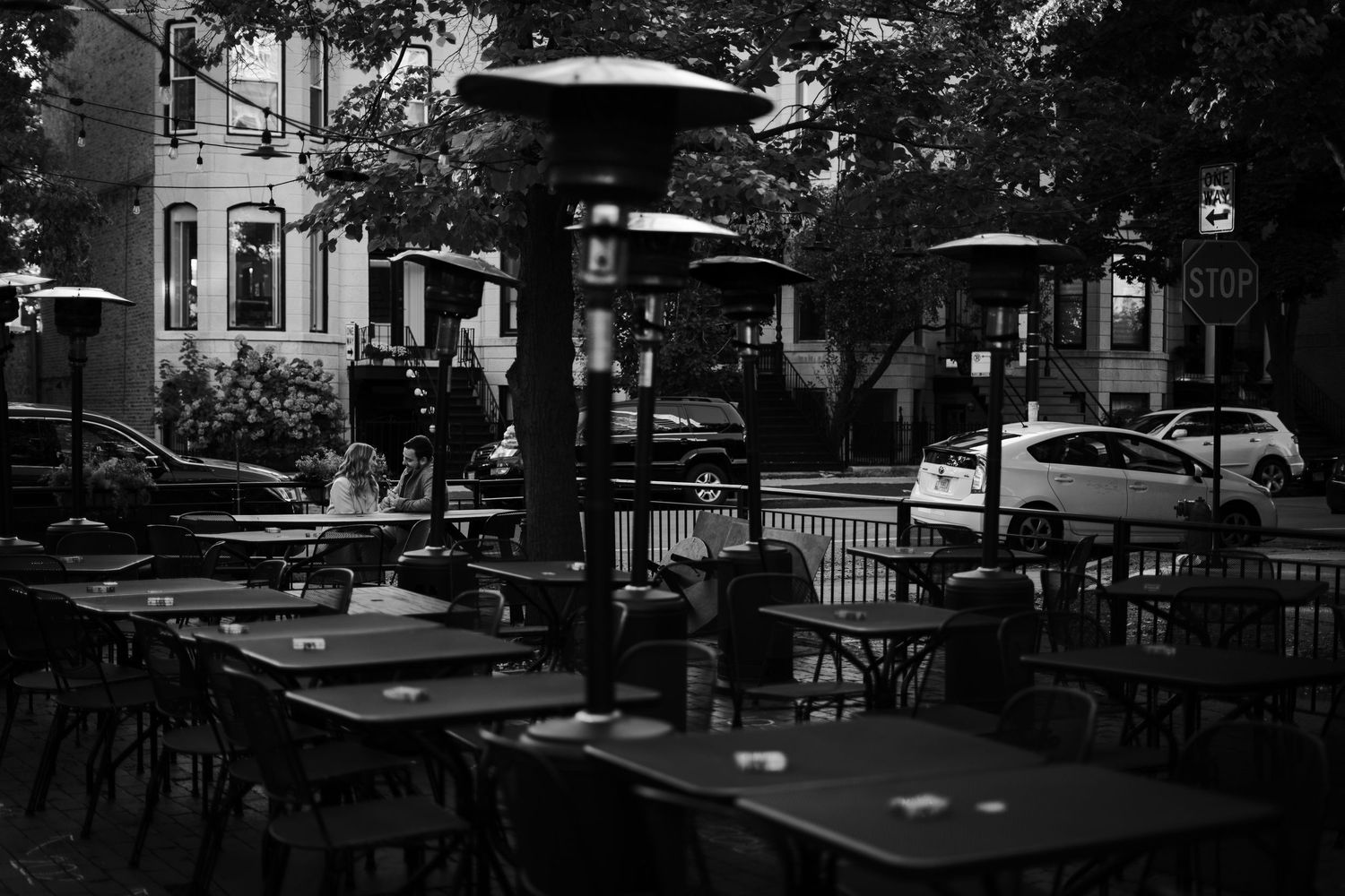 Empty outdoor patio restaurant with heaters and umbrella tables in black and white urban setting.