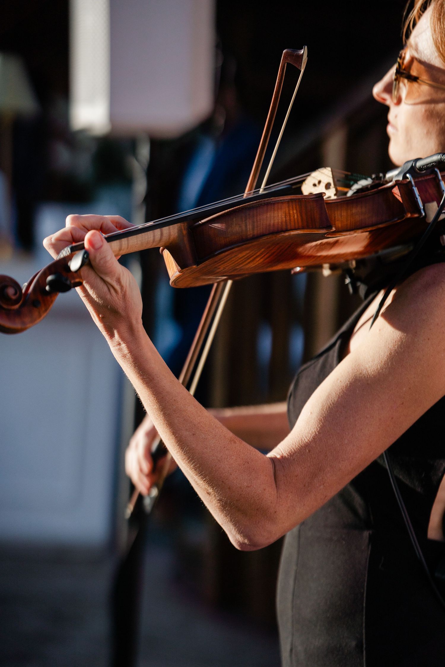 Close-up of a woman in black dress playing violin at an outdoor wedding ceremony.
