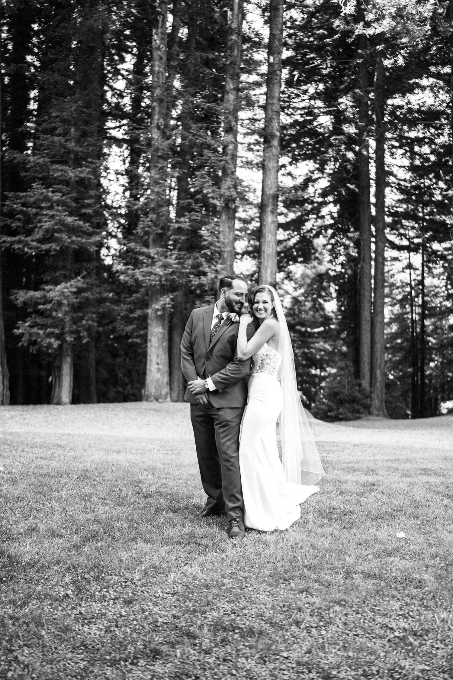 Black and white photo of bride and groom embracing in a forest clearing on their wedding day.