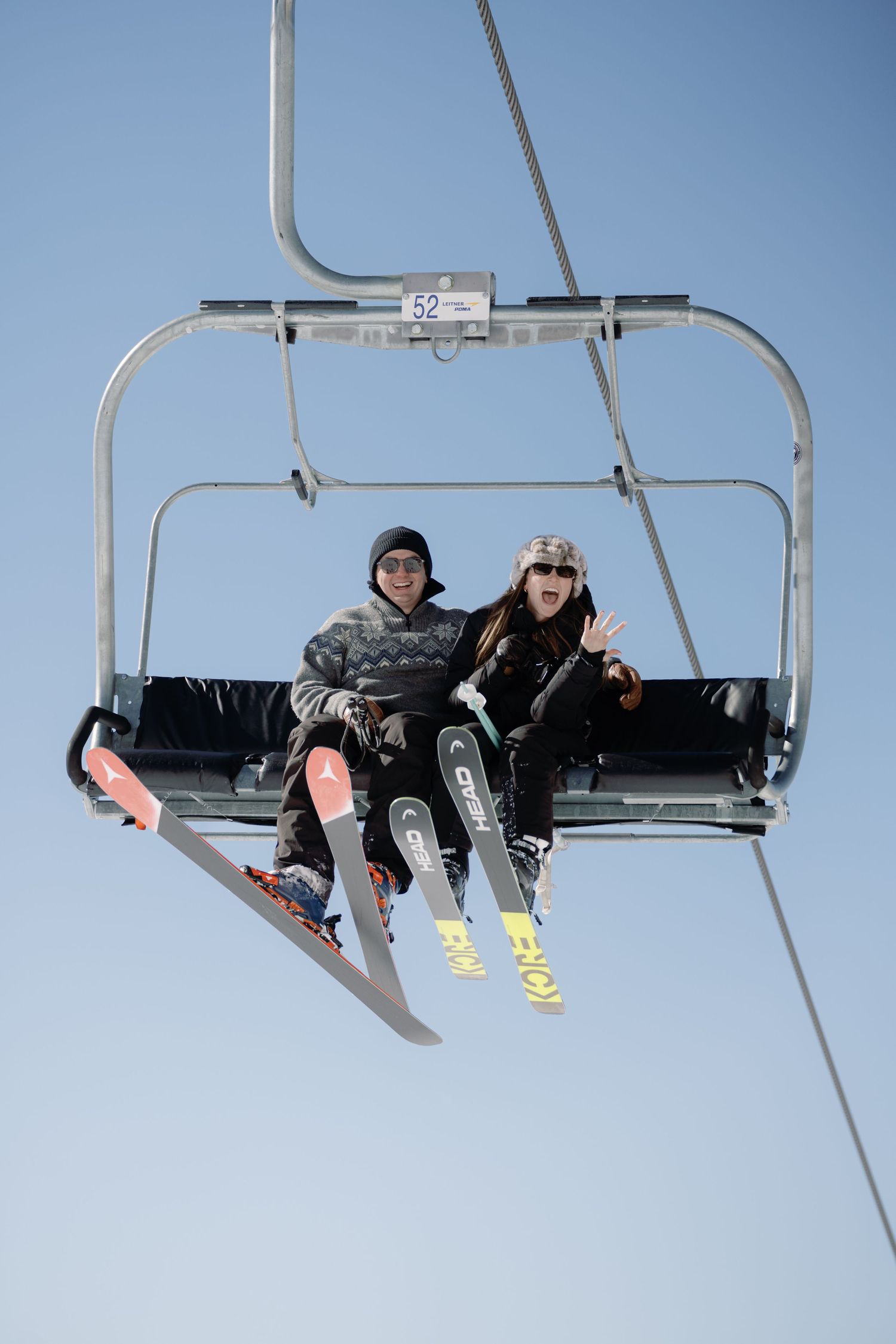 Two skiers on chairlift number 52 posing against a clear blue sky.