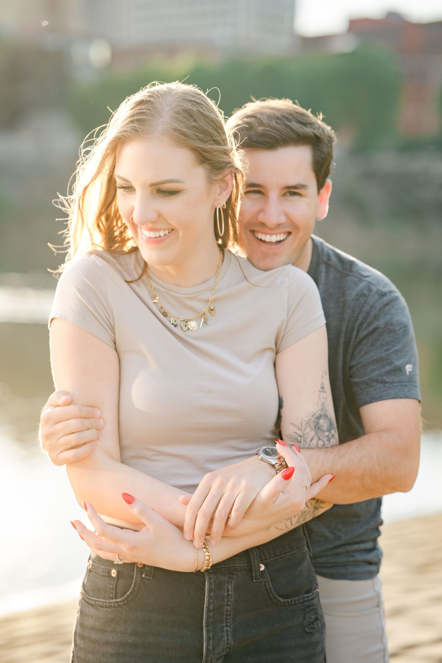 Smiling couple embracing outdoors in golden hour light near a waterfront urban setting.