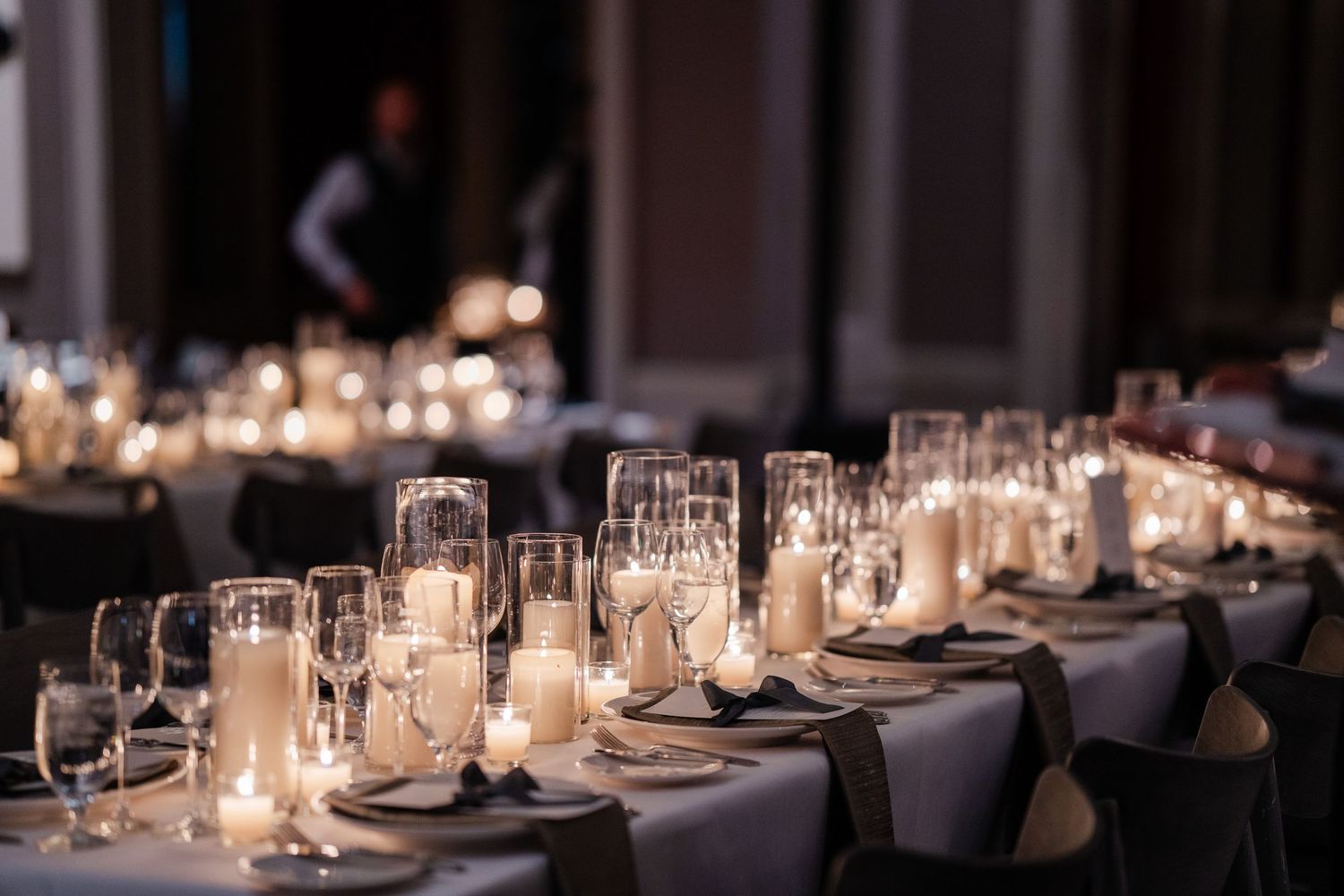 Elegant wedding reception table set with glowing candles, crystal glassware, and white linens.