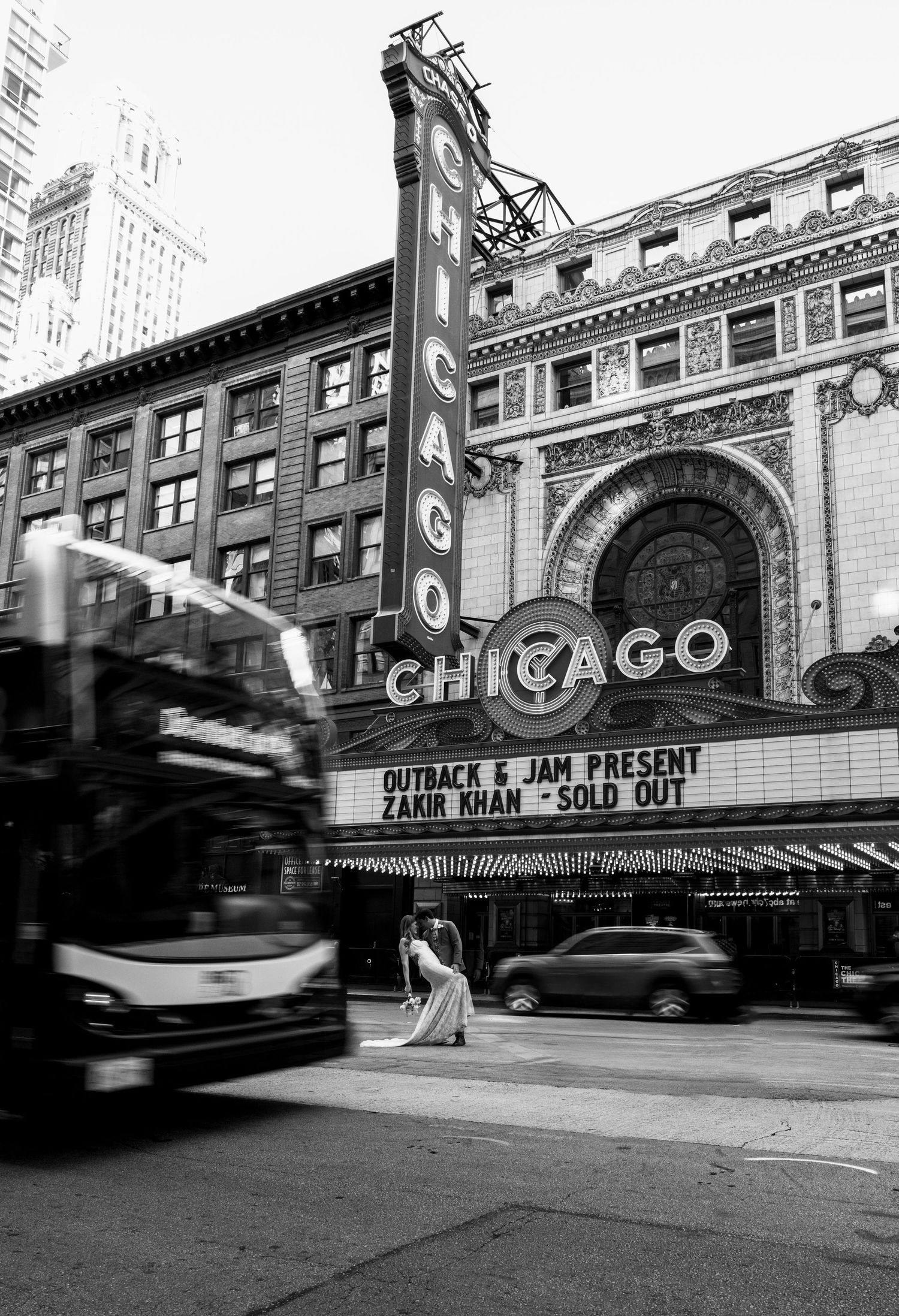 Bride poses in wedding gown in front of iconic Chicago Theatre marquee with city traffic.