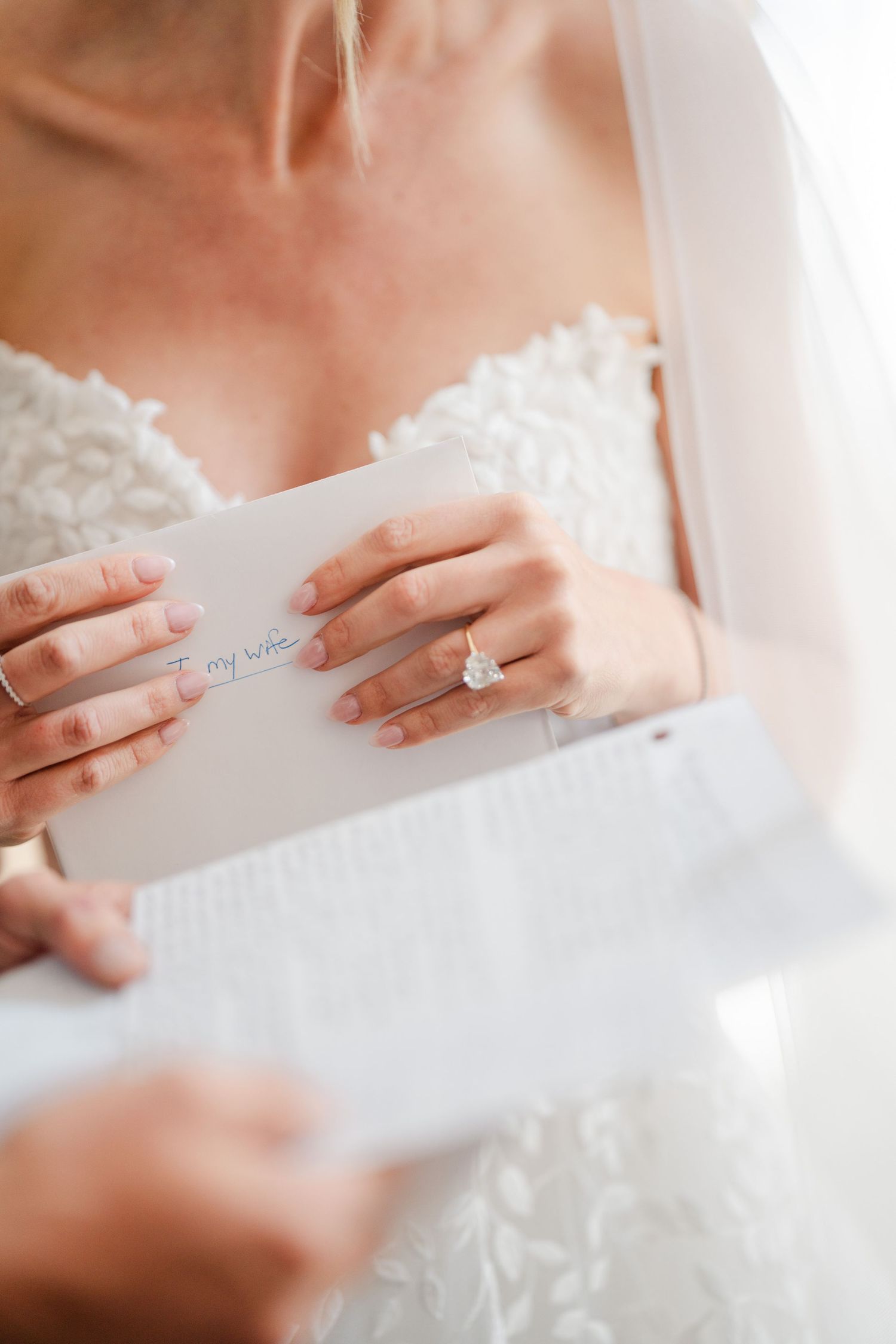 Bride in lace wedding dress reading a heartfelt letter addressed to my wife while wearing diamond engagement ring.