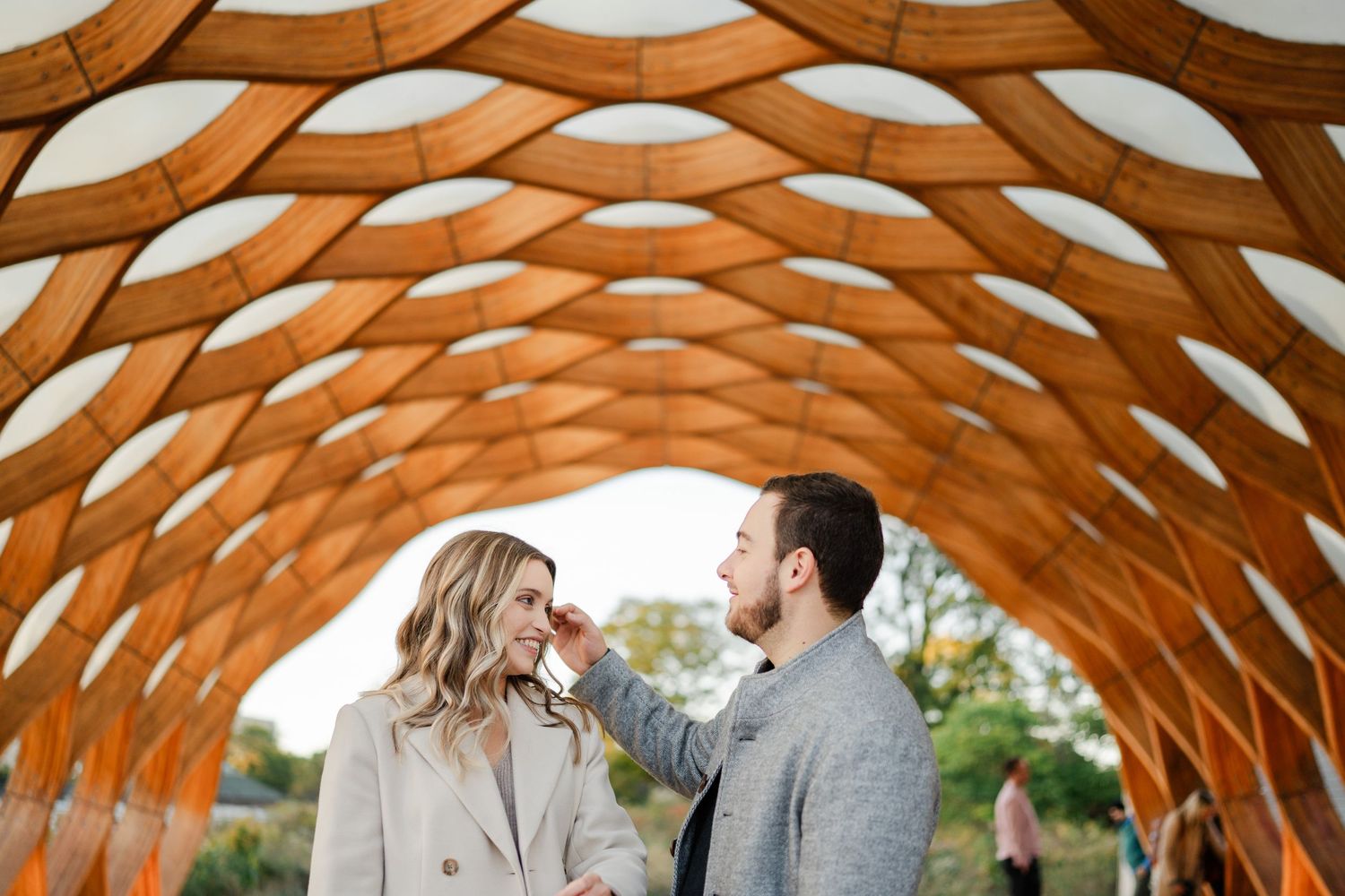 Smiling engaged couple sharing a playful moment under the iconic honeycomb pavilion in Lincoln Park.