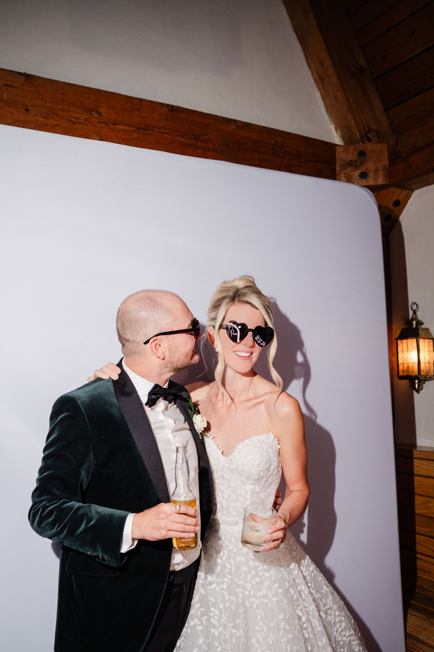 Bride and groom wearing sunglasses holding drinks at wedding photo booth.