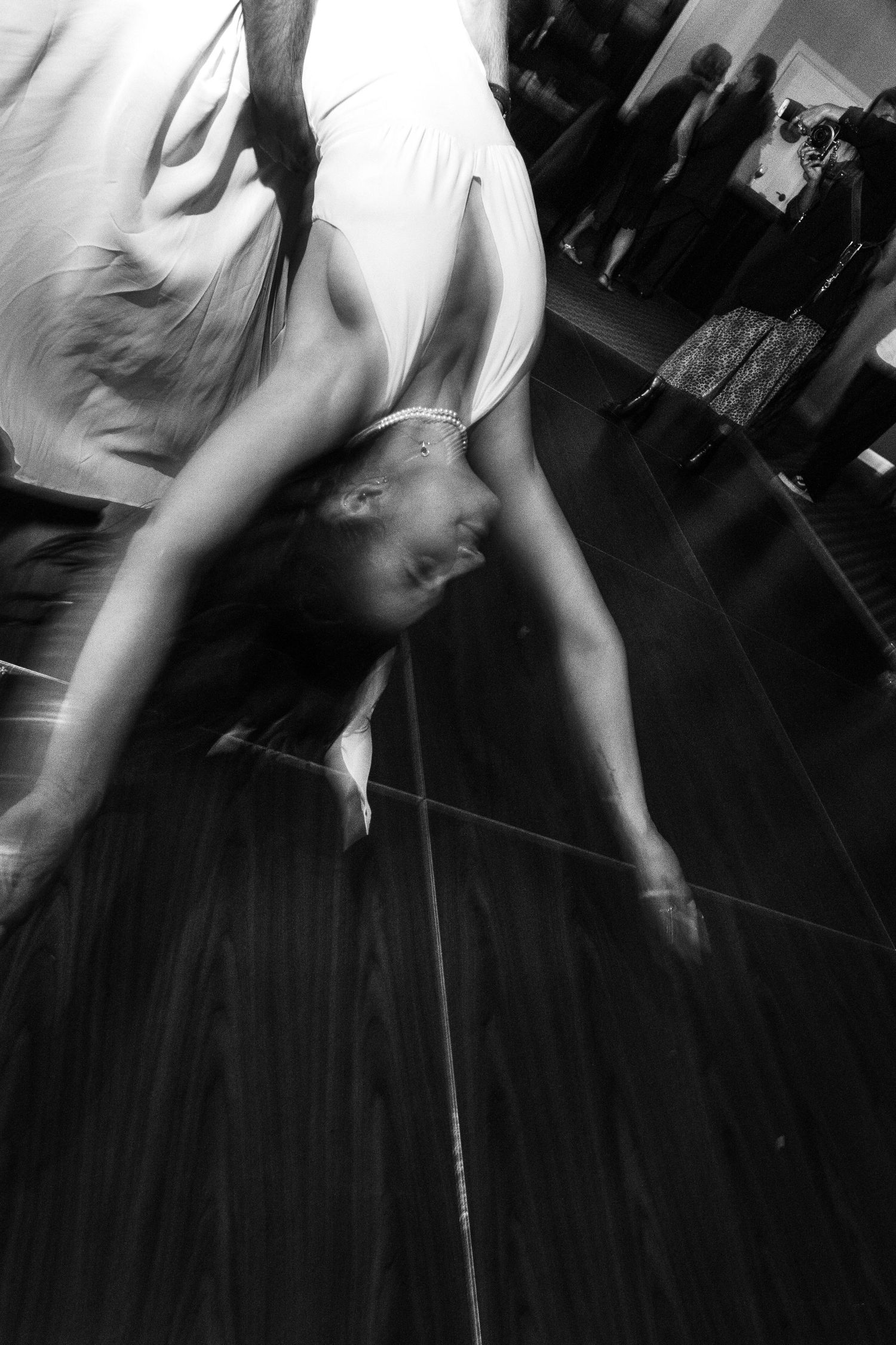 Black and white photo of a bride bending over backwards on a wooden dance floor at a wedding reception.