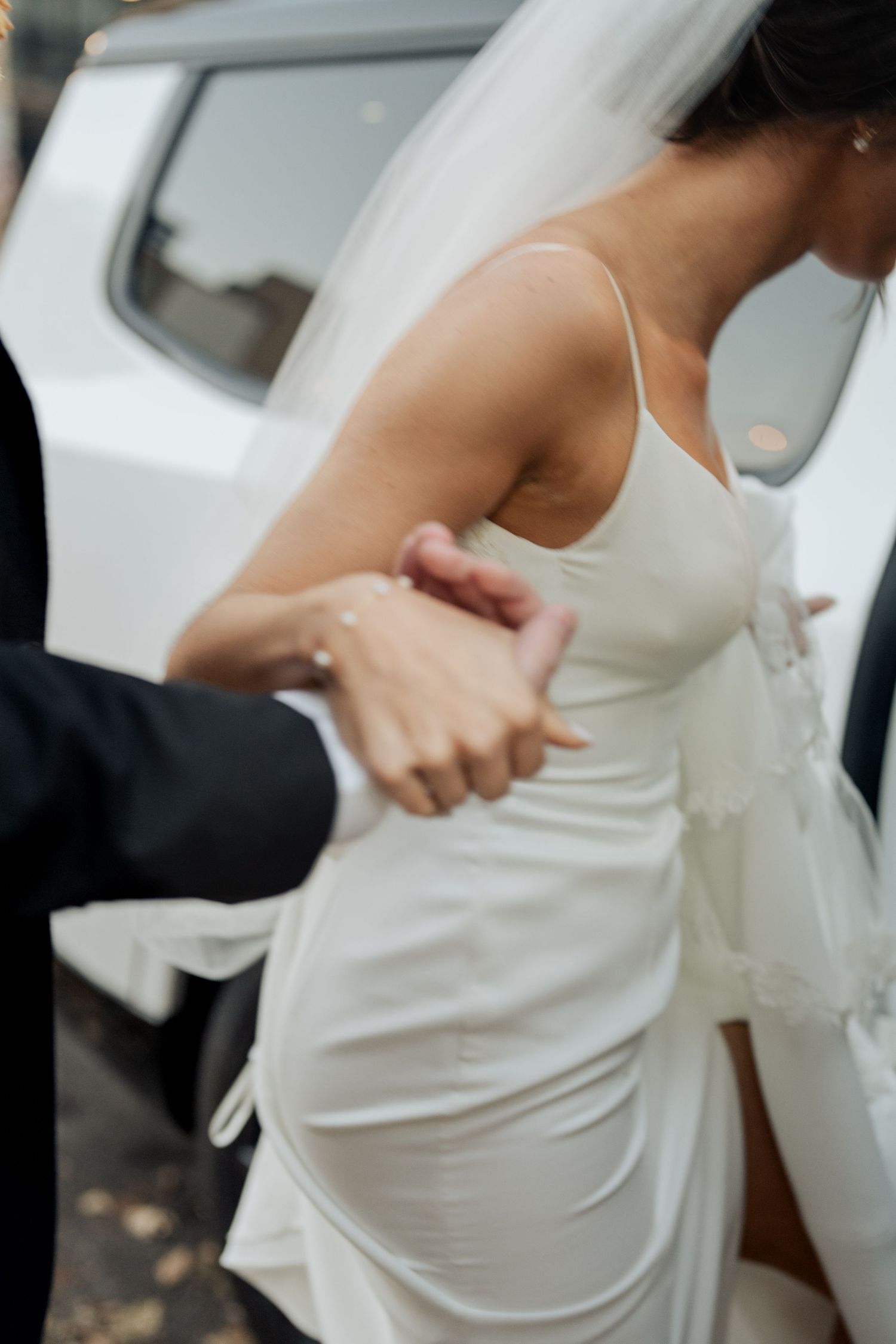 Groom tenderly holding bride's hand as she exits a white vehicle in her wedding dress.