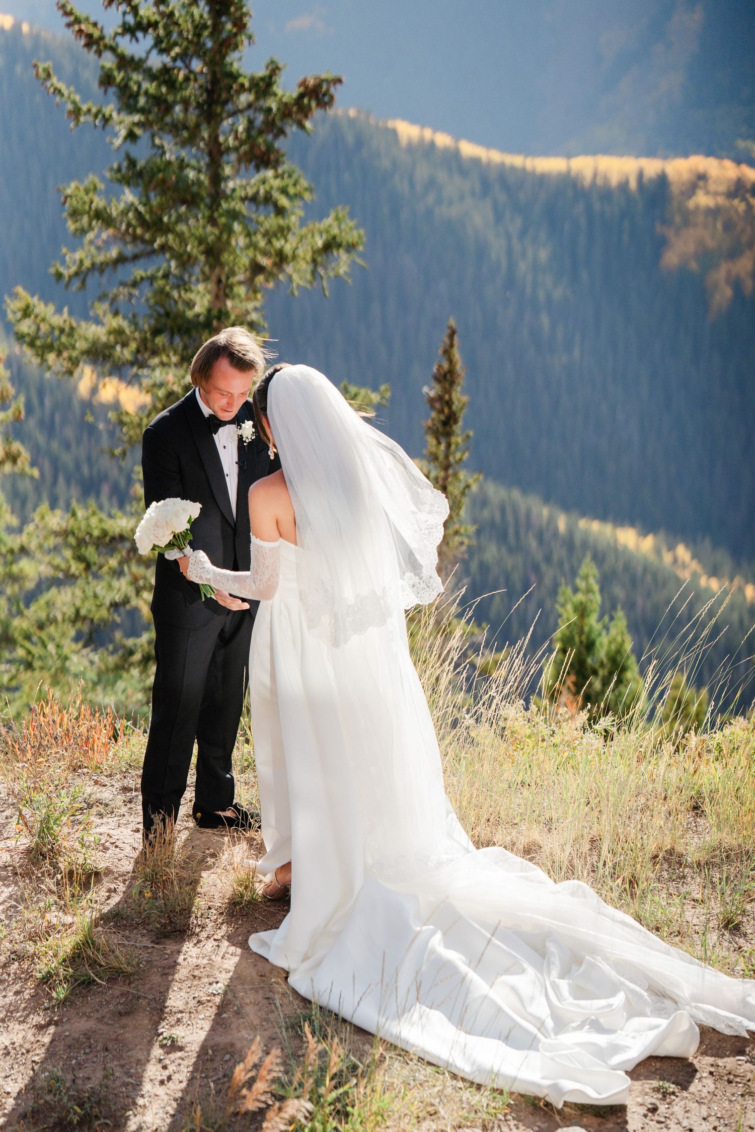 Bride and groom share an intimate moment reading vows on a scenic mountain overlook surrounded by pine trees.