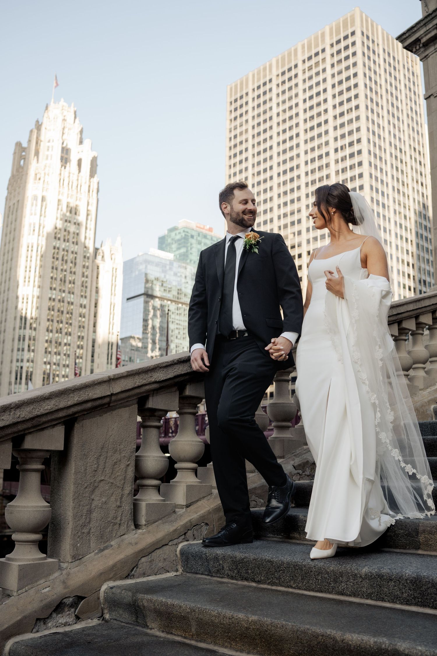 Bride and groom descending stone steps with Chicago Tribune Tower skyline in background.