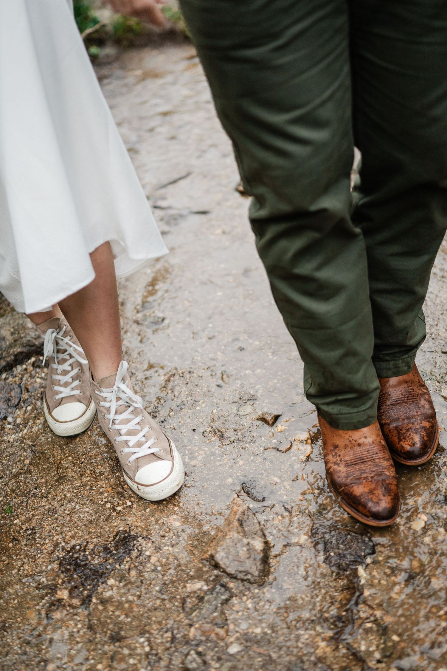Close-up of couples feet showing womans white Converse sneakers and mans brown leather boots on rocky ground.