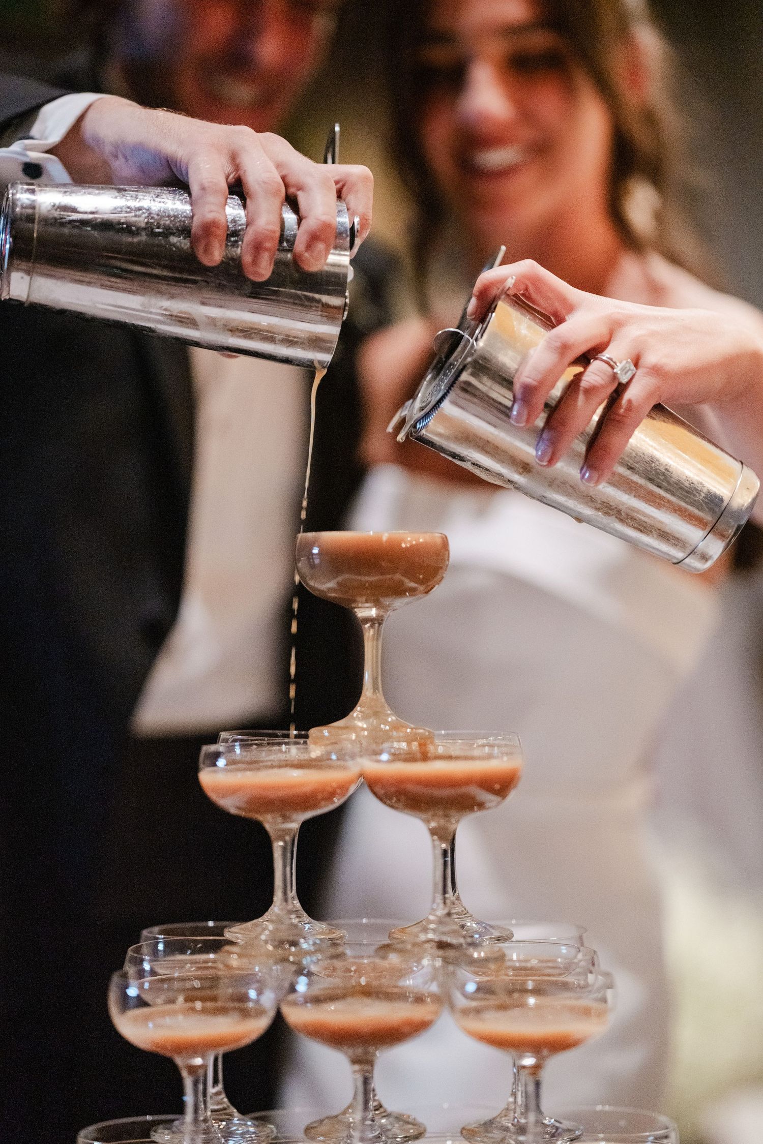 Bride and groom pour espresso martinis over a champagne tower at their wedding reception.