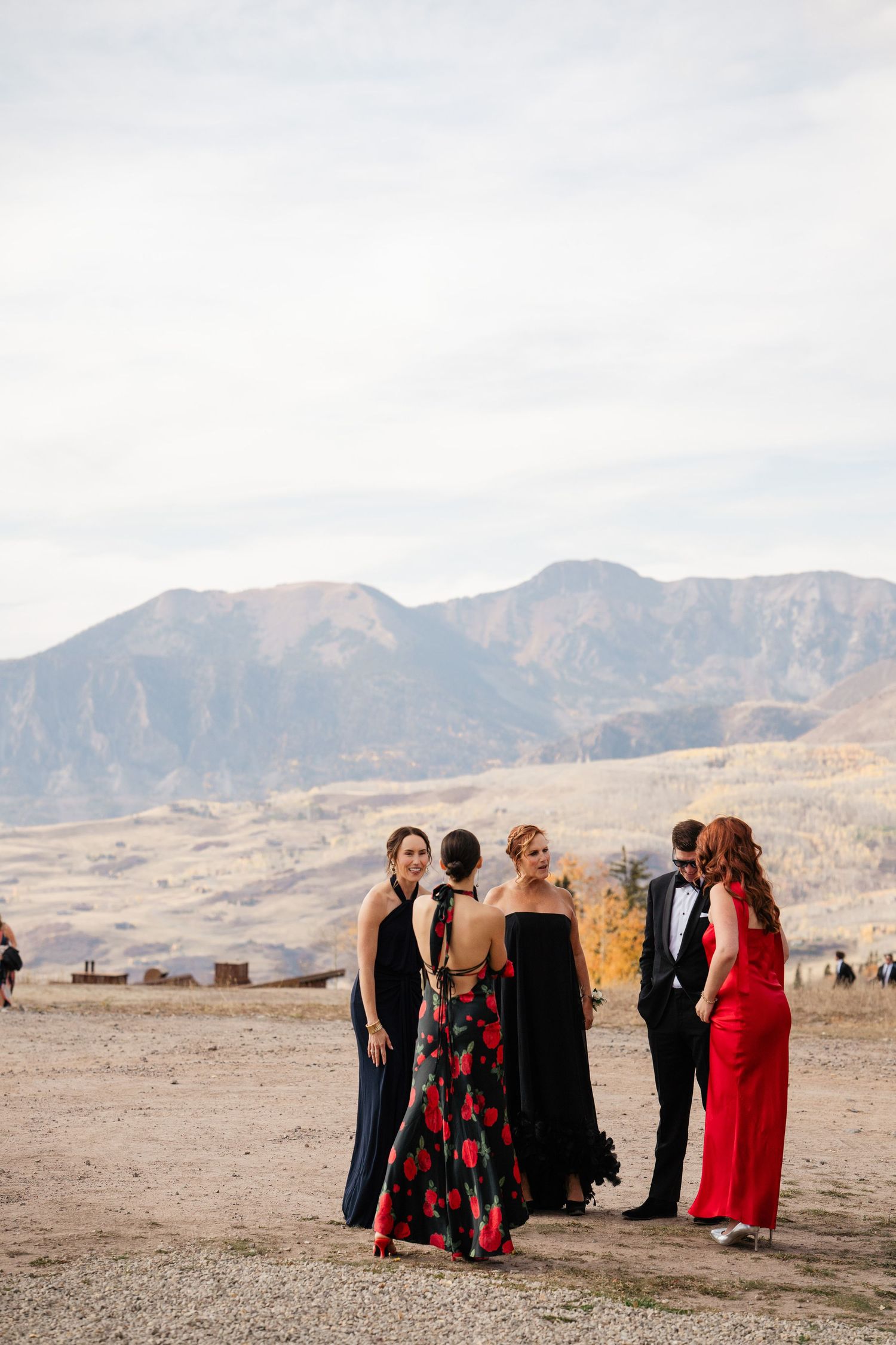 Wedding guests in formal attire socializing outdoors with stunning mountain range backdrop in autumn.