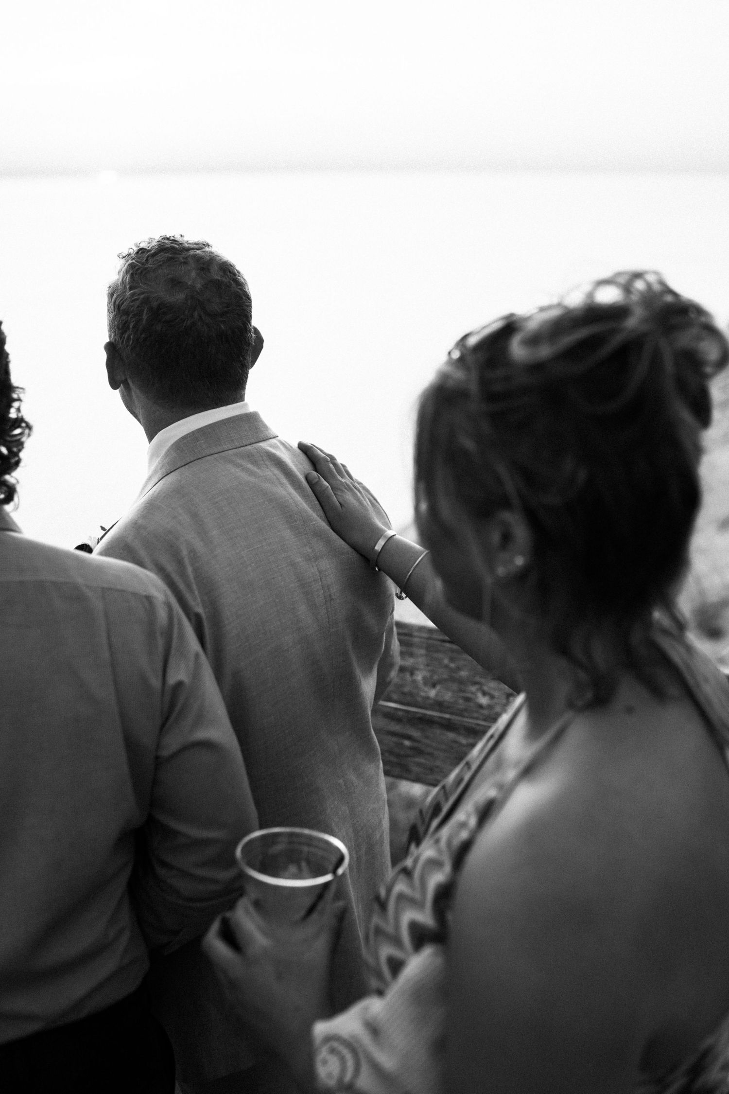 Black and white photo of wedding guests gazing at a waterfront view during a reception.