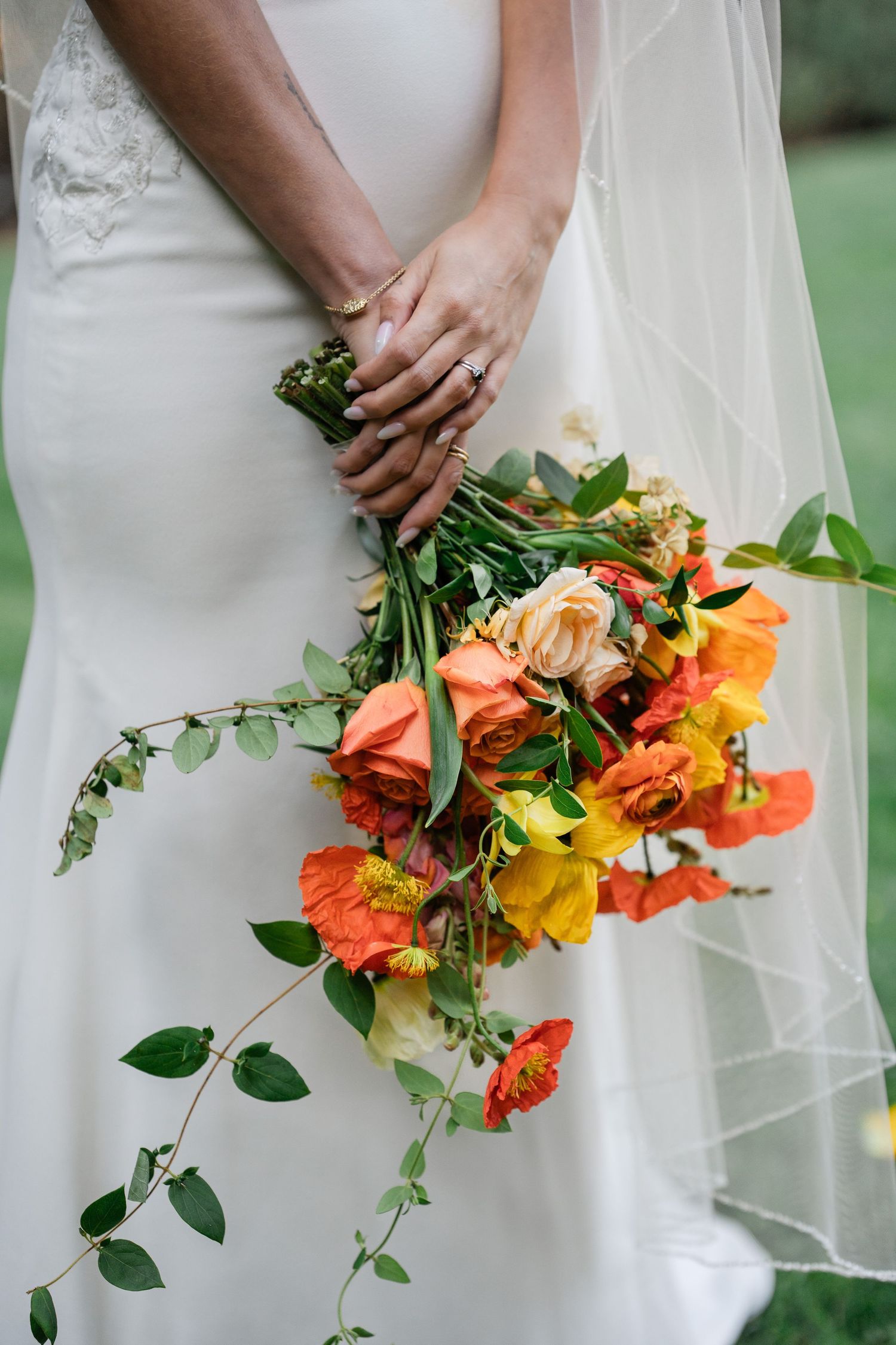 Bride holding vibrant orange and peach bridal bouquet with greenery against white wedding gown.