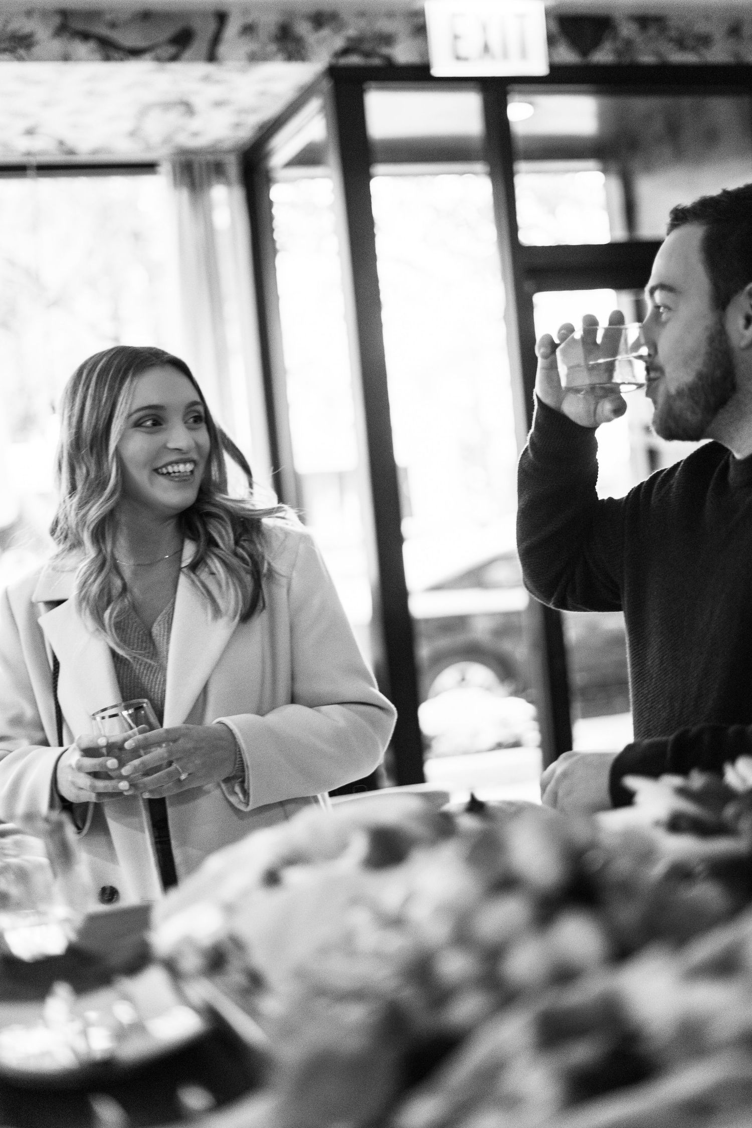 Couple sharing drinks and laughing together at a restaurant in black and white engagement photo.