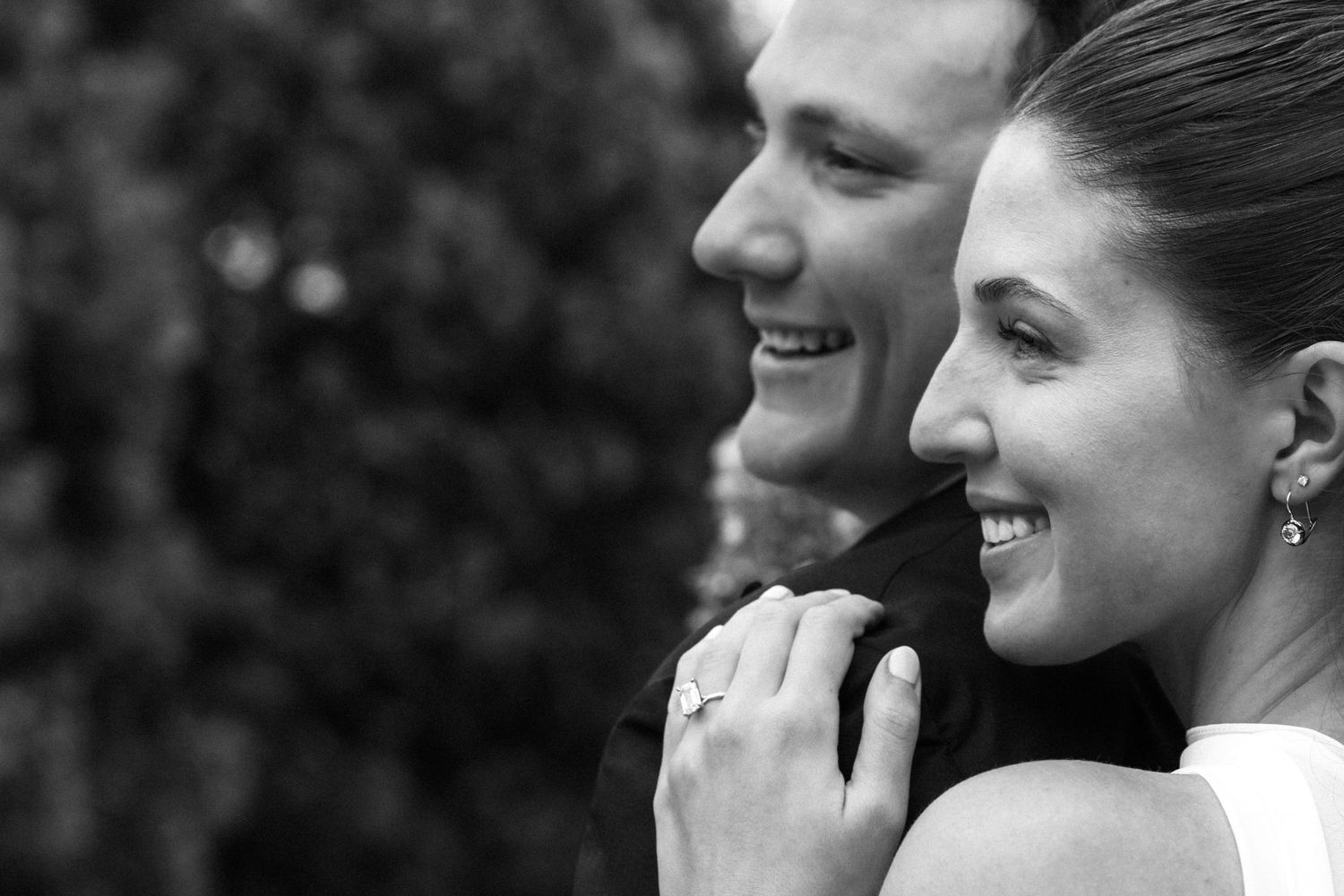 Black and white close-up of smiling bride and groom sharing a tender moment, bride showing off engagement ring.