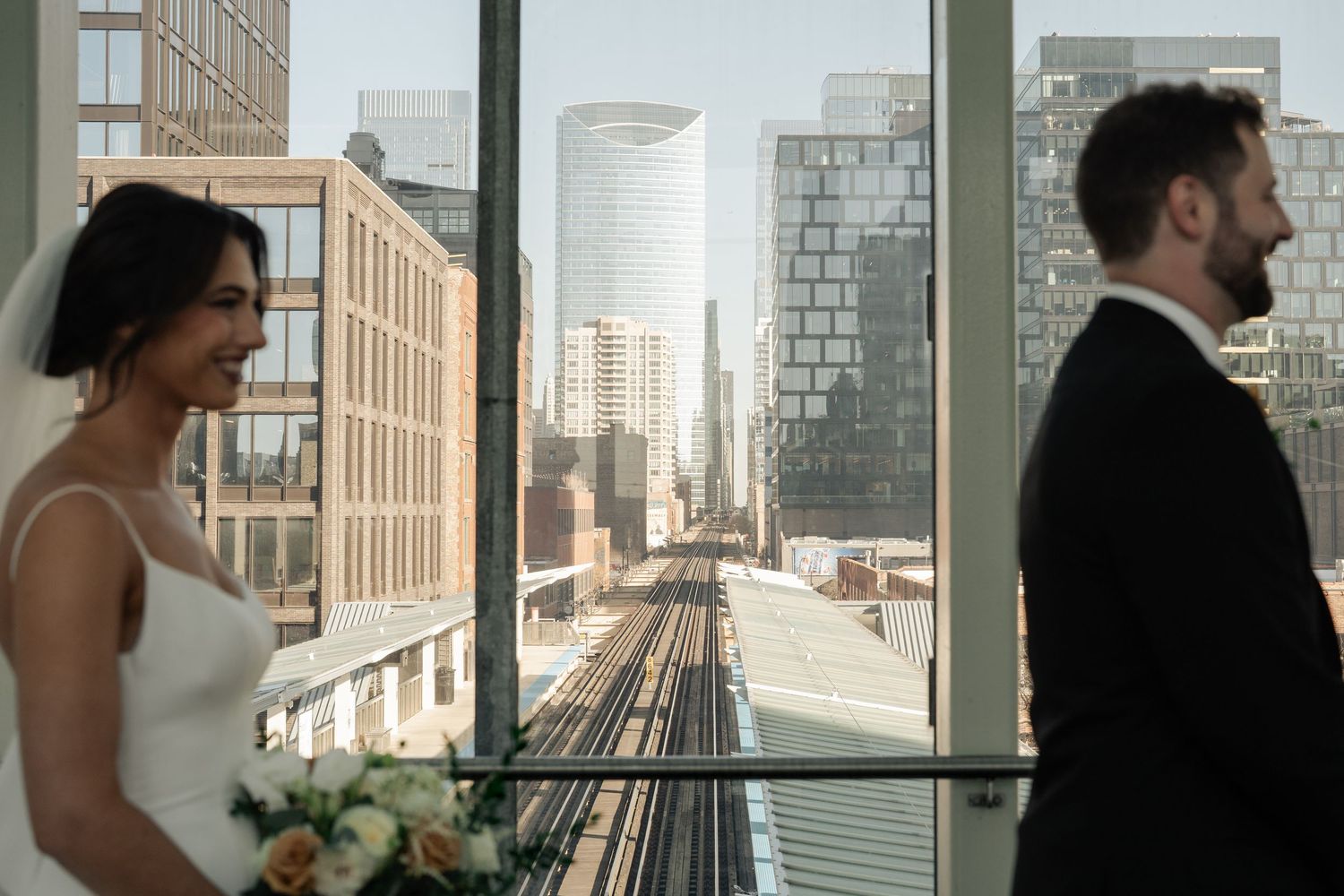 Bride and groom share romantic moment by window overlooking Chicago elevated train tracks.