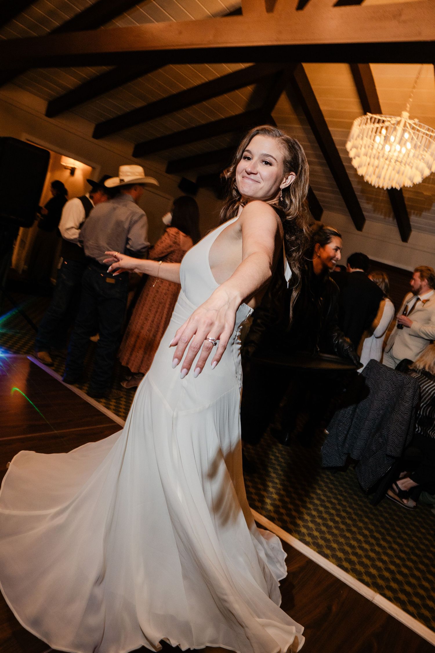 Bride in white halter gown twirling on dance floor at rustic wedding reception.