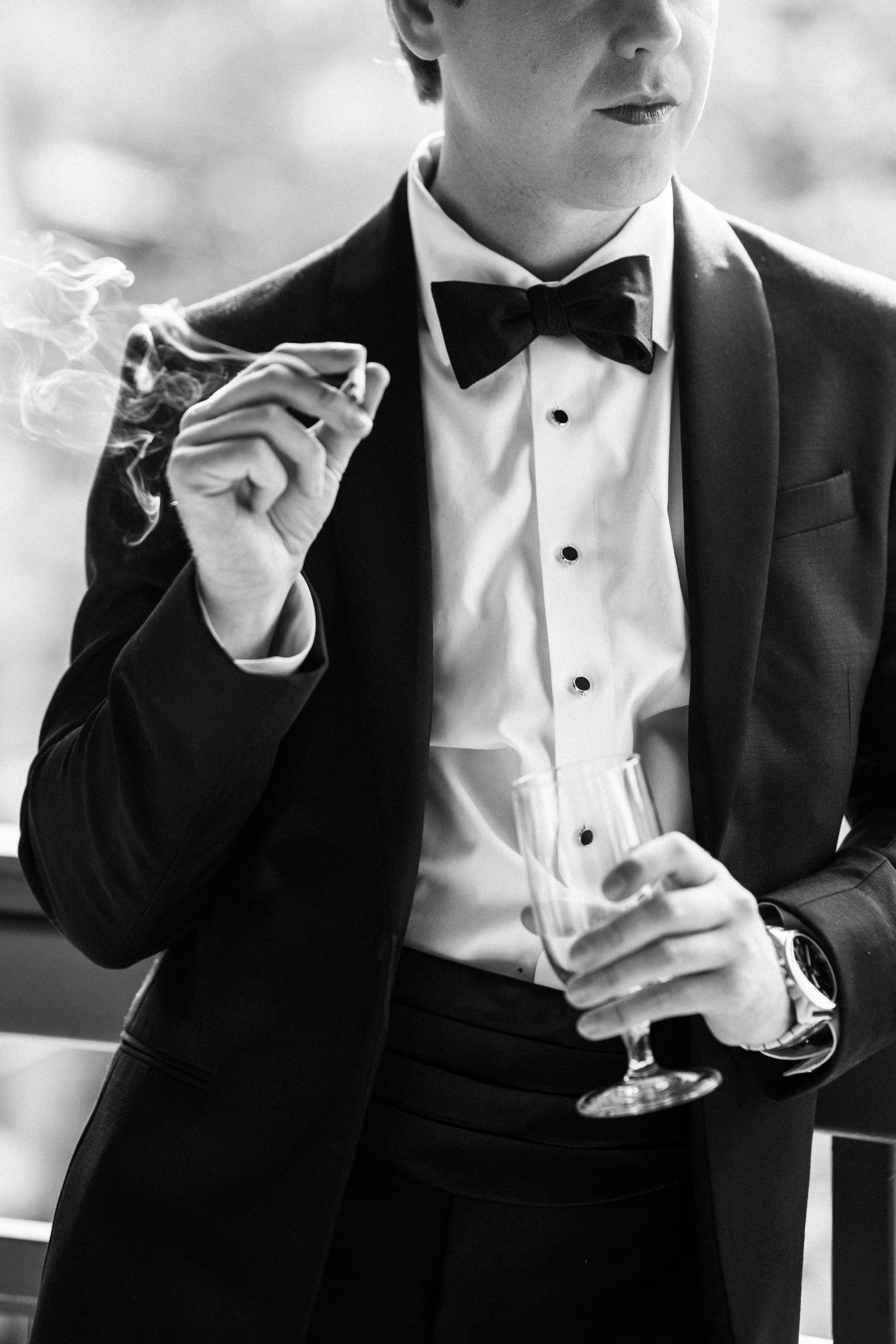 Black and white photo of groom in tuxedo holding champagne glass and cigar.