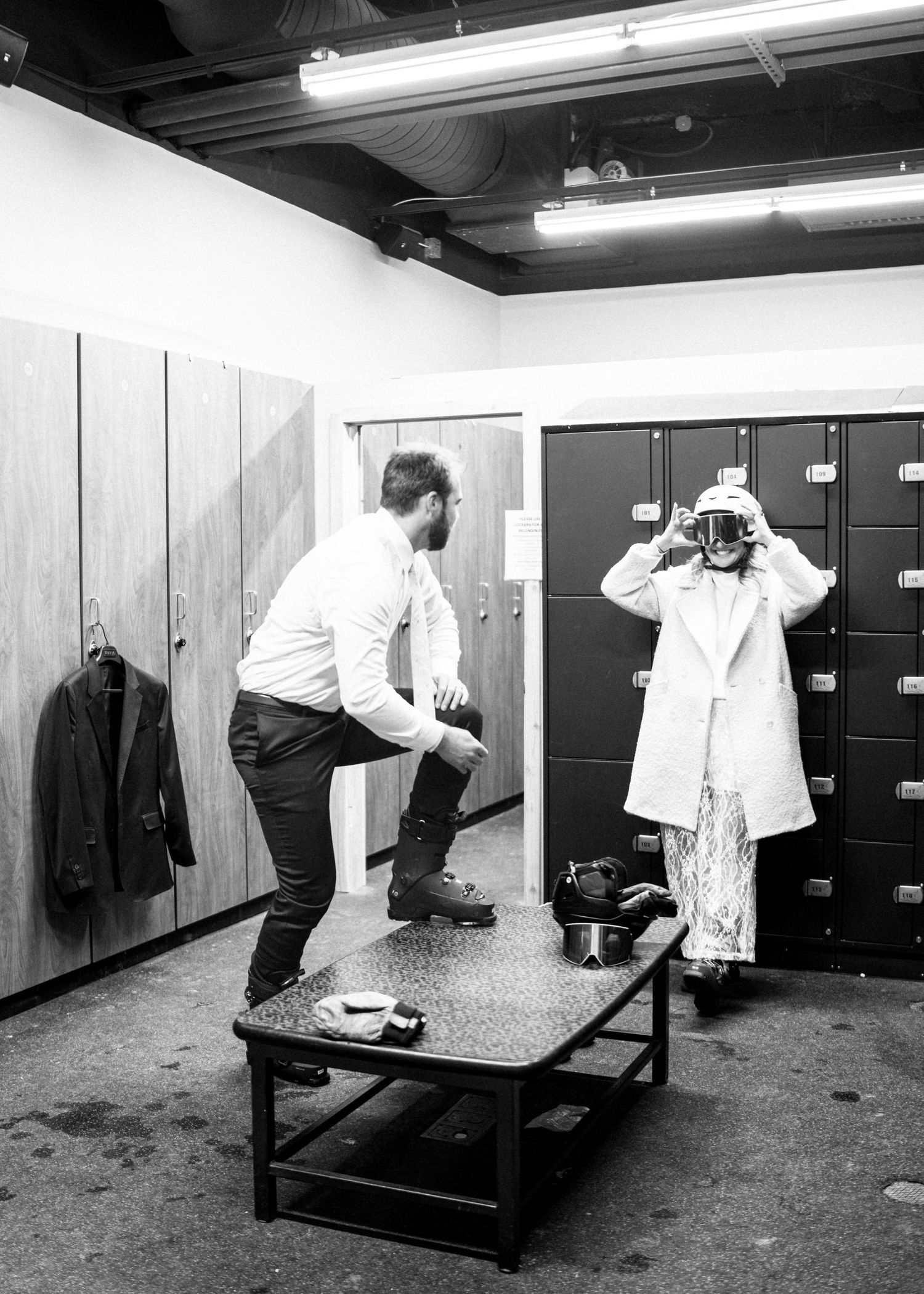 Couple trying on ski helmets and goggles in a ski resort locker room, black and white.