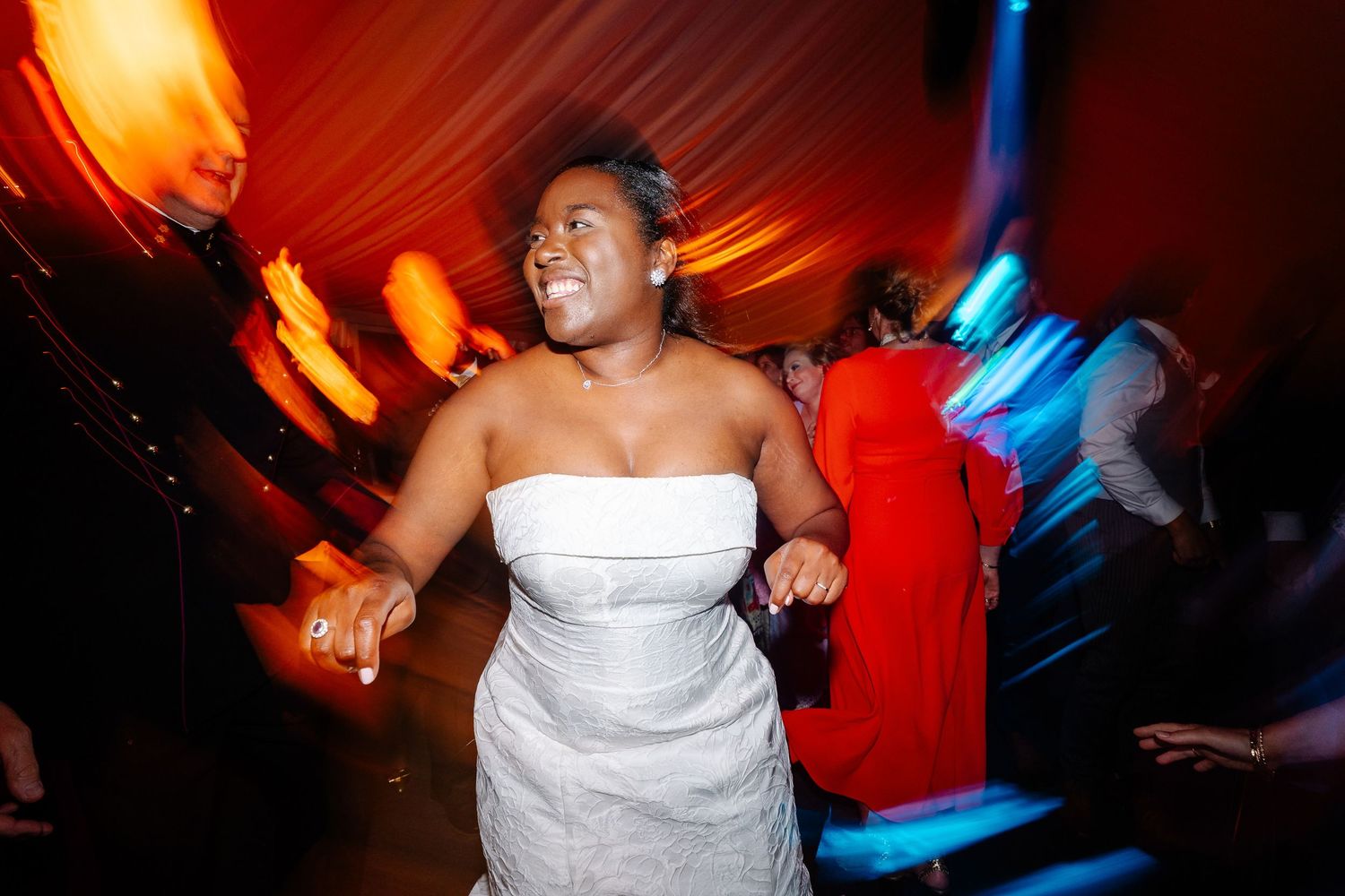 Guests dancing and celebrating at a wedding reception with colorful red and blue lighting effects.