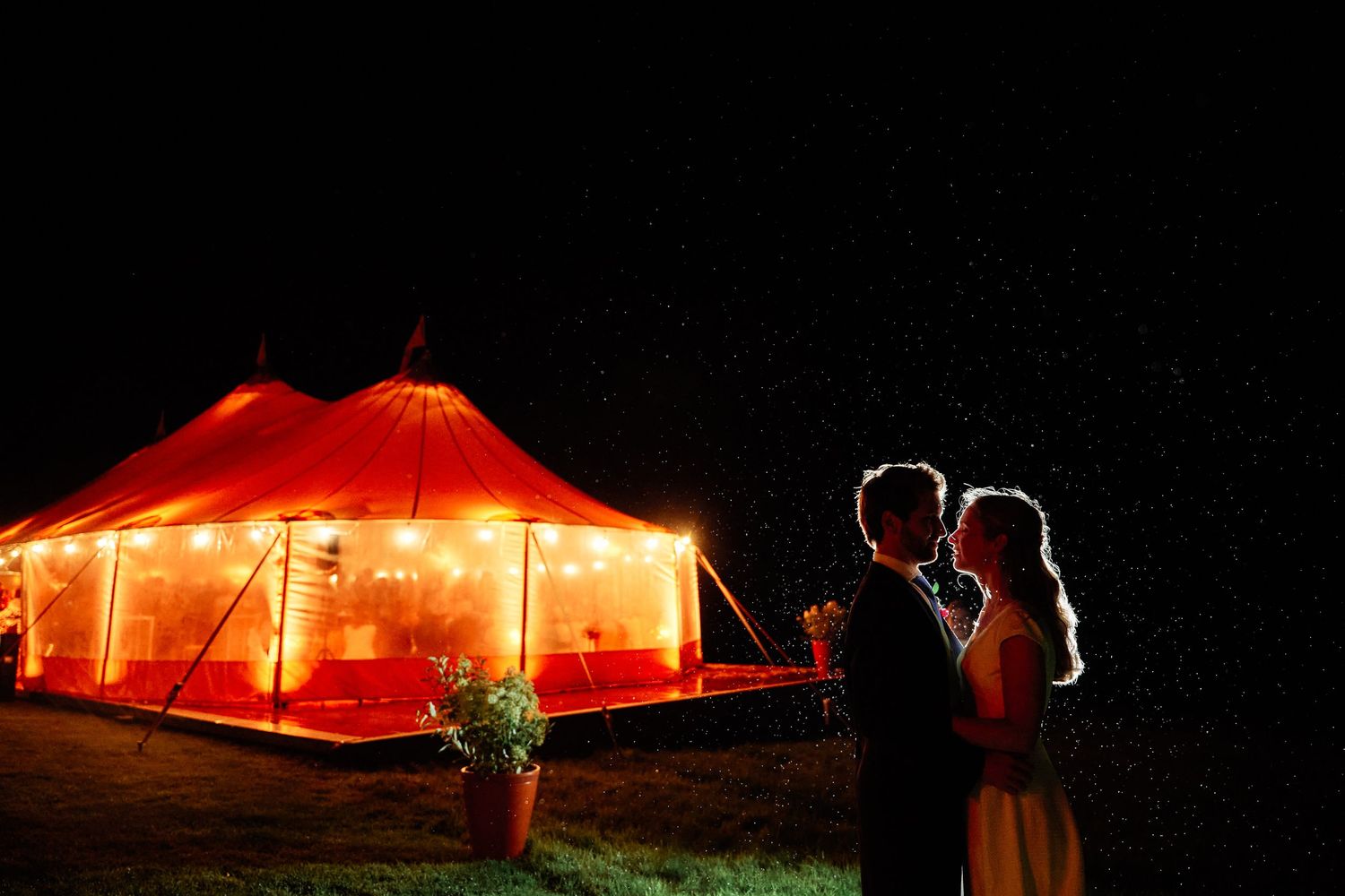 Red illuminated tent glows against dark night sky with multiple connected sections creating dramatic lighting effect.