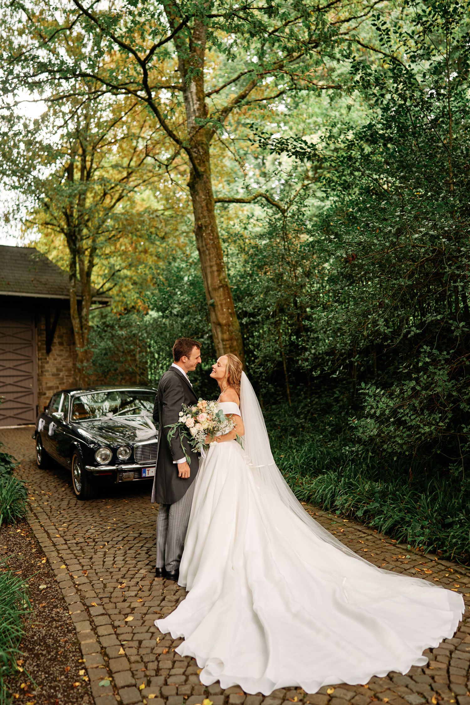 A romantic wedding photo sequence showing a couple with a classic vintage car on a cobblestone path surrounded by autumn trees.