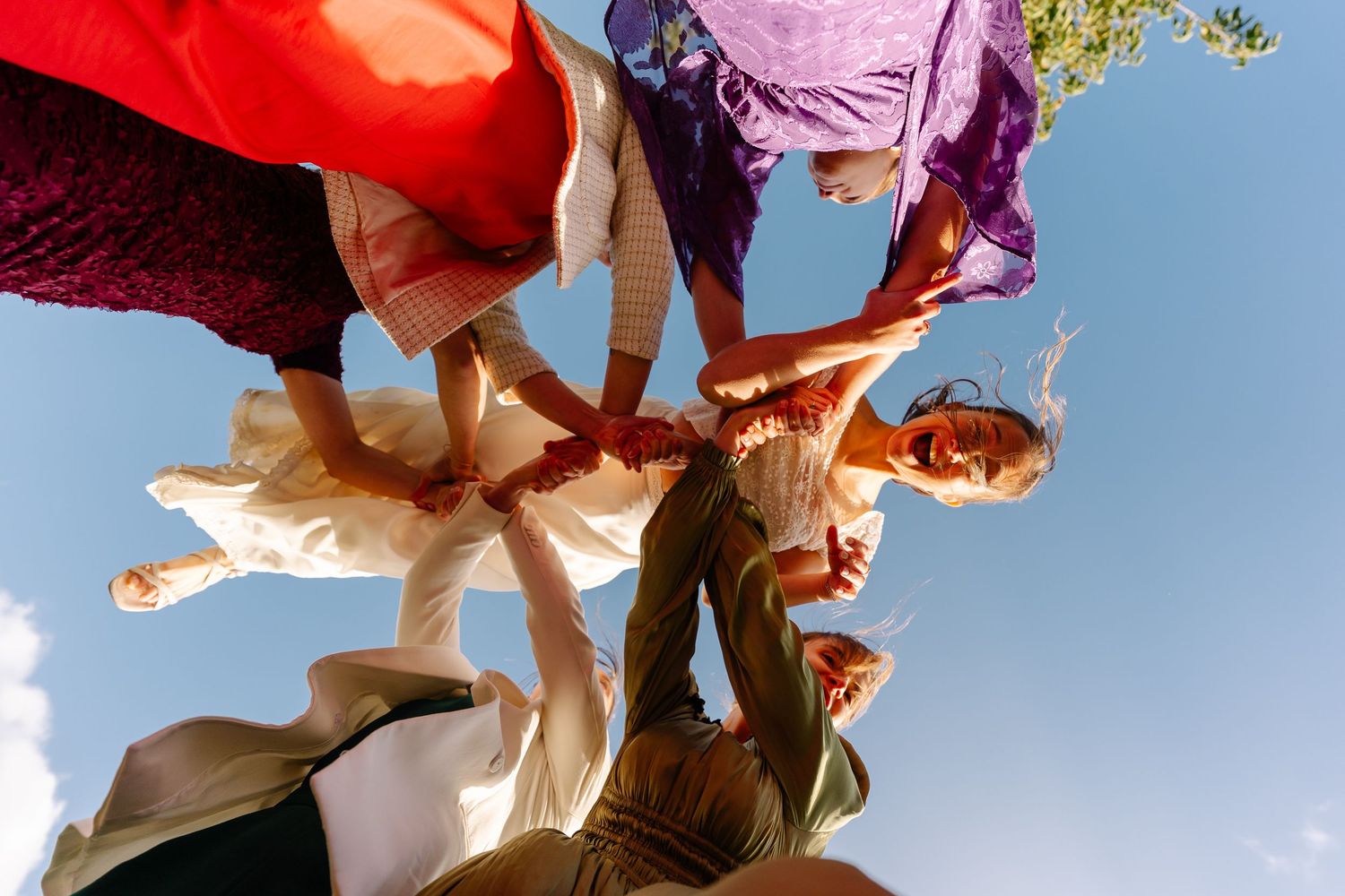 A group of people in colorful clothing huddle together in a circle formation against a bright blue sky.