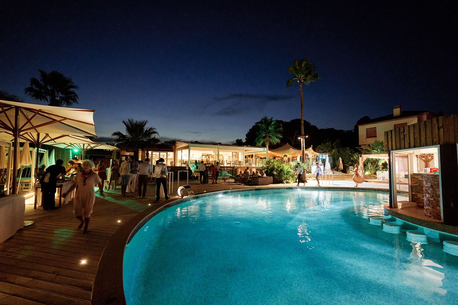 Illuminated resort swimming pool at night with glowing blue water and ambient lighting creating a tranquil atmosphere.