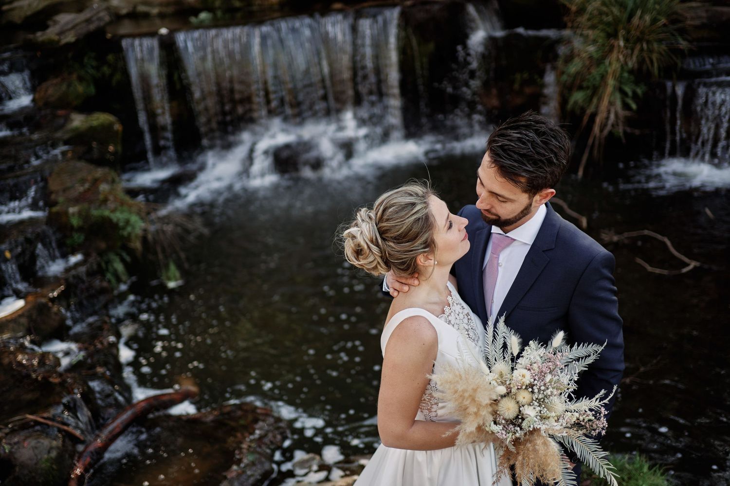 A couple shares a romantic moment by a cascading waterfall during their wedding ceremony.