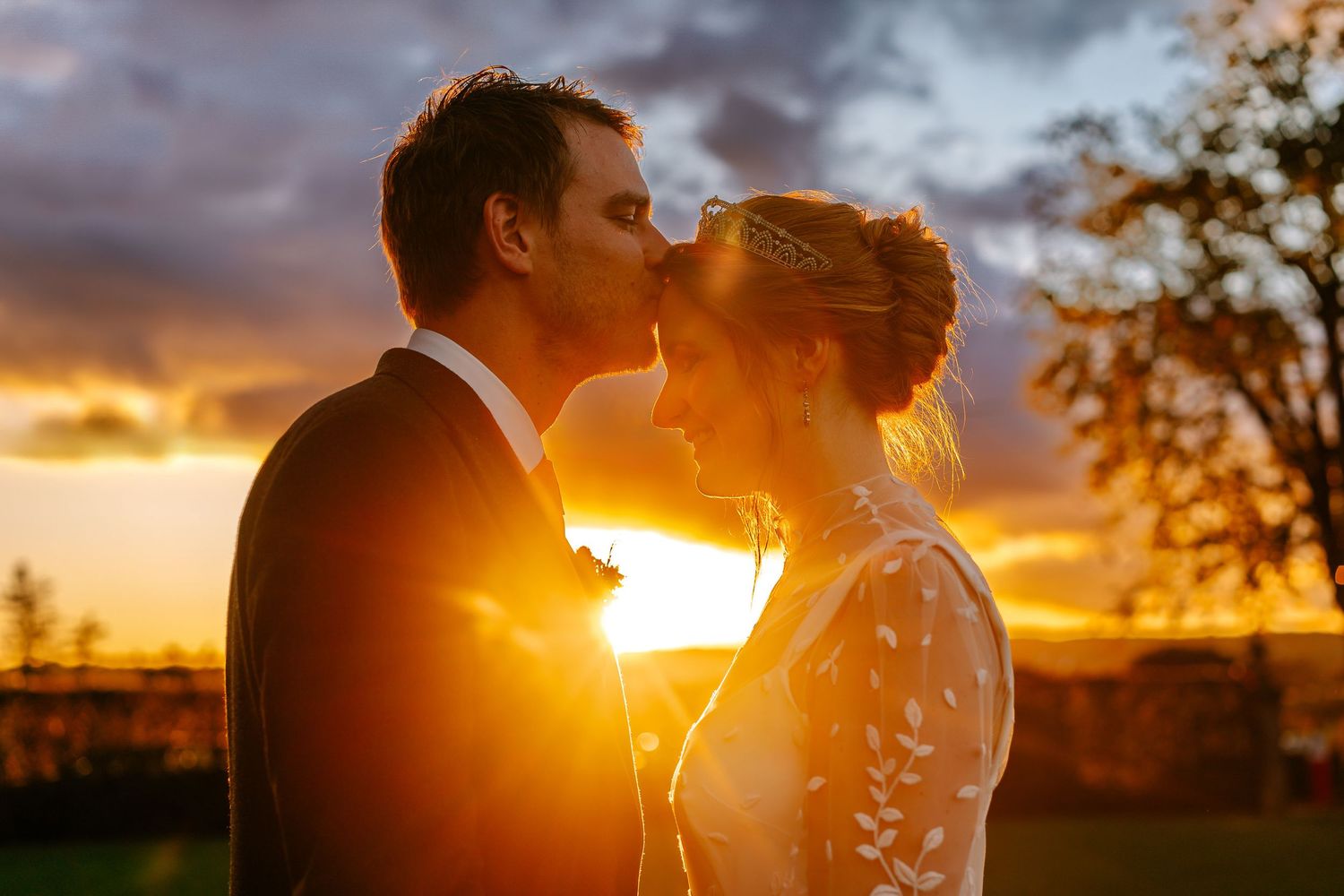 Silhouetted couple embraces during a vibrant orange sunset with sun rays streaming between them.