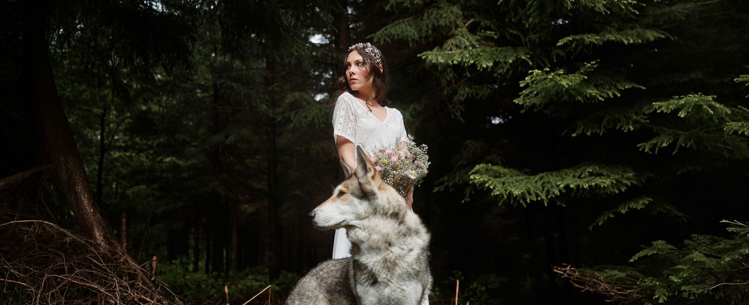 A wedding couple poses in a lush forest setting surrounded by towering evergreen trees.