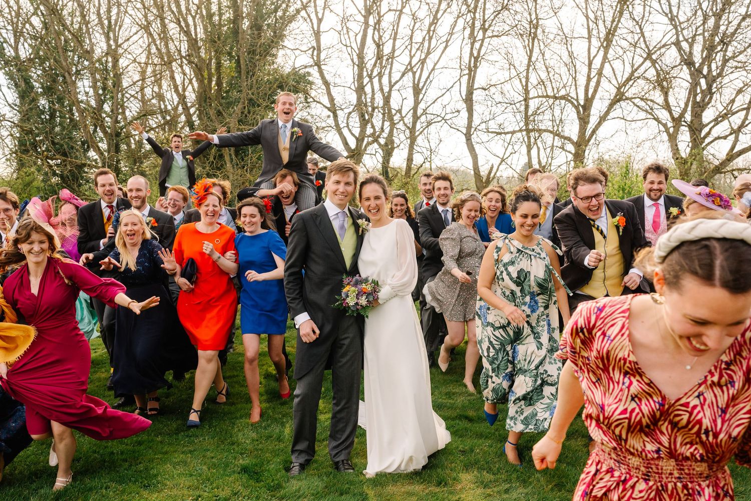 Wedding guests form a circle and dance together in a joyful celebration outdoors during a spring day.