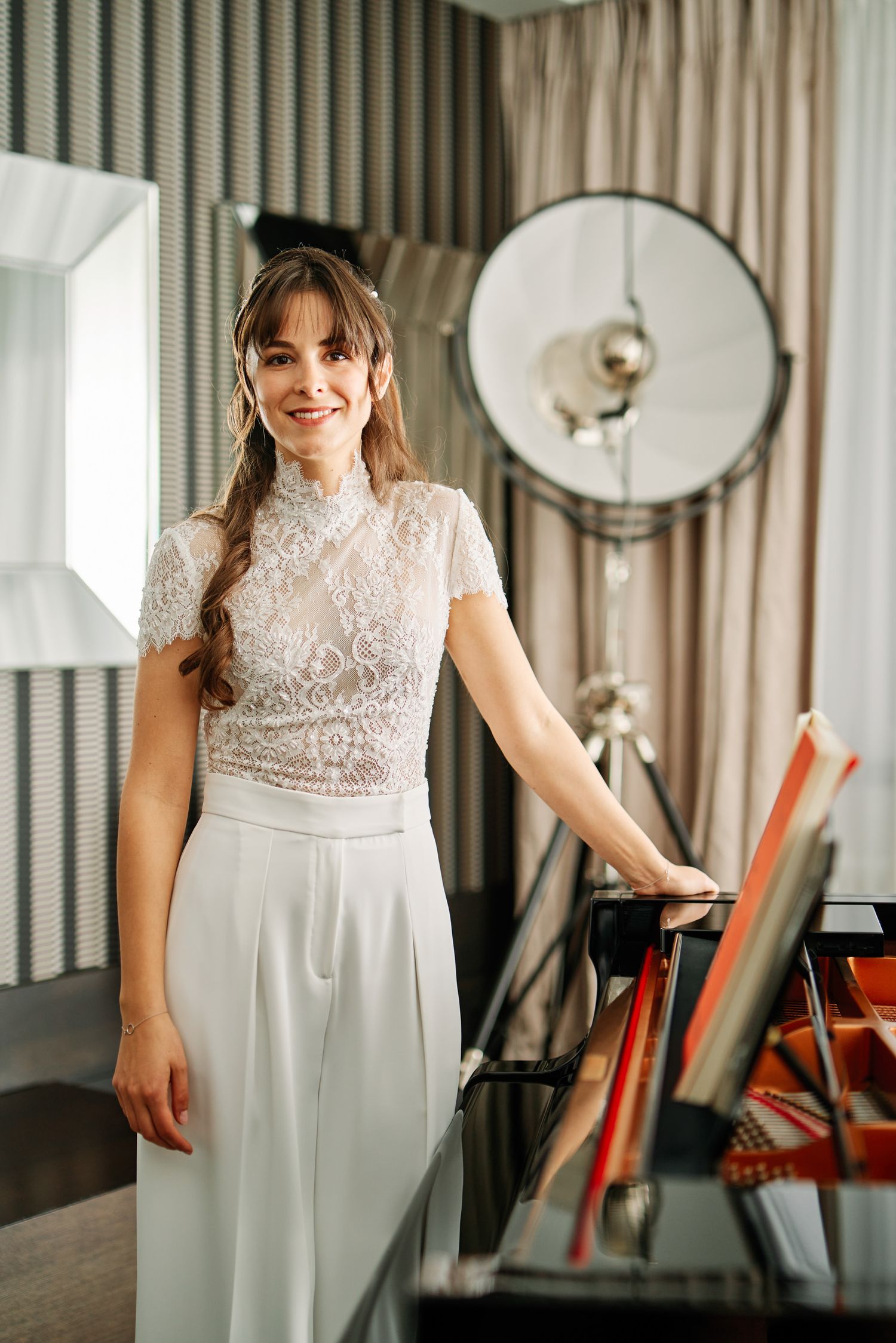 Elegant white lace wedding dress with high neck and cap sleeves shown in a room with studio lighting equipment.