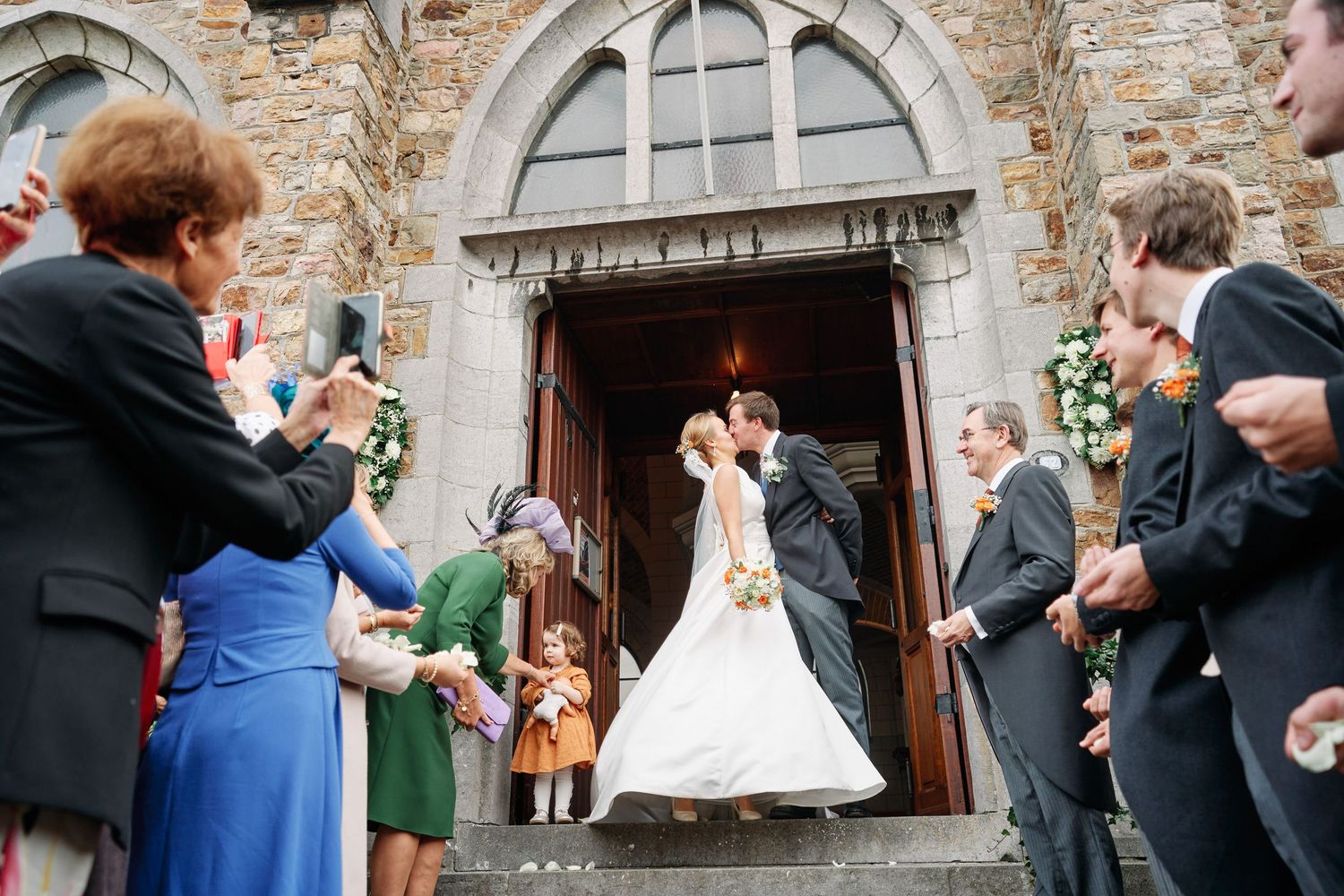 Wedding guests line up outside a historic stone church entrance to greet the newlyweds after their ceremony.