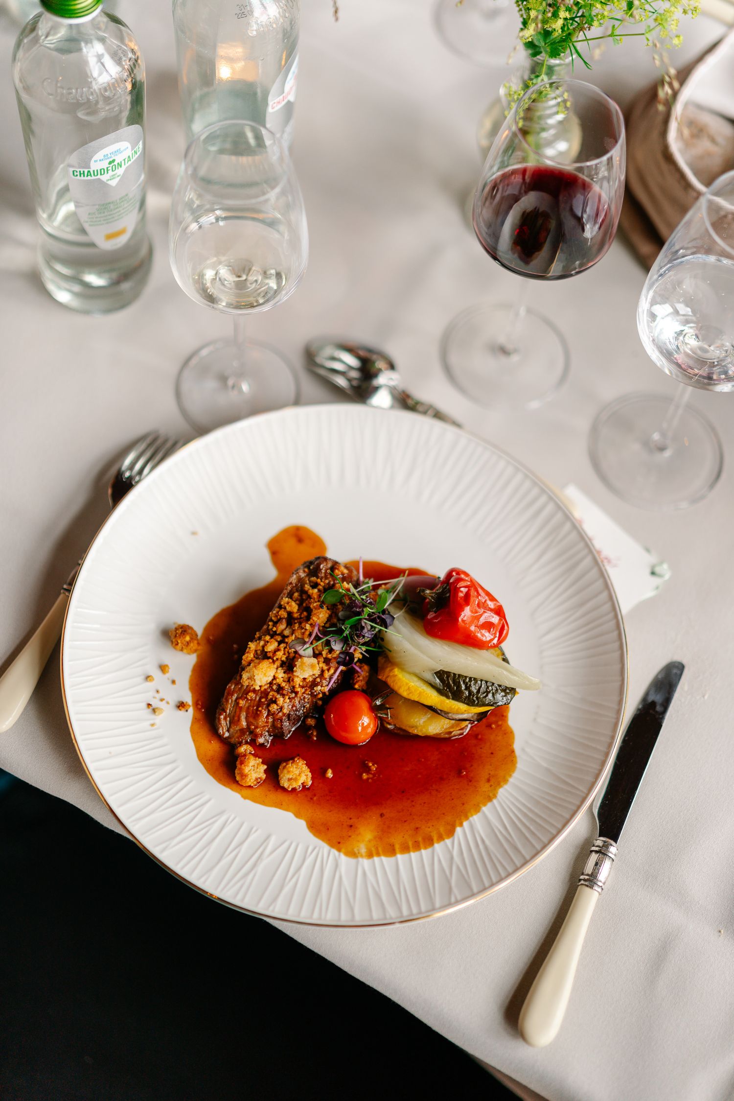 Elegant plated dishes with colorful sauces and garnishes served on white plates in an upscale restaurant setting.