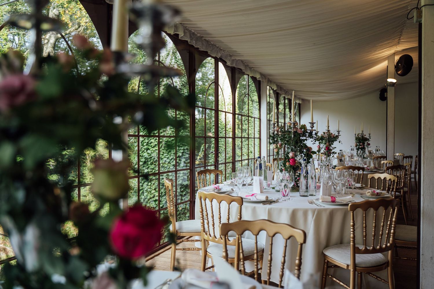 Elegant wedding reception venue with white tablecloths and tall windows overlooking lush greenery.