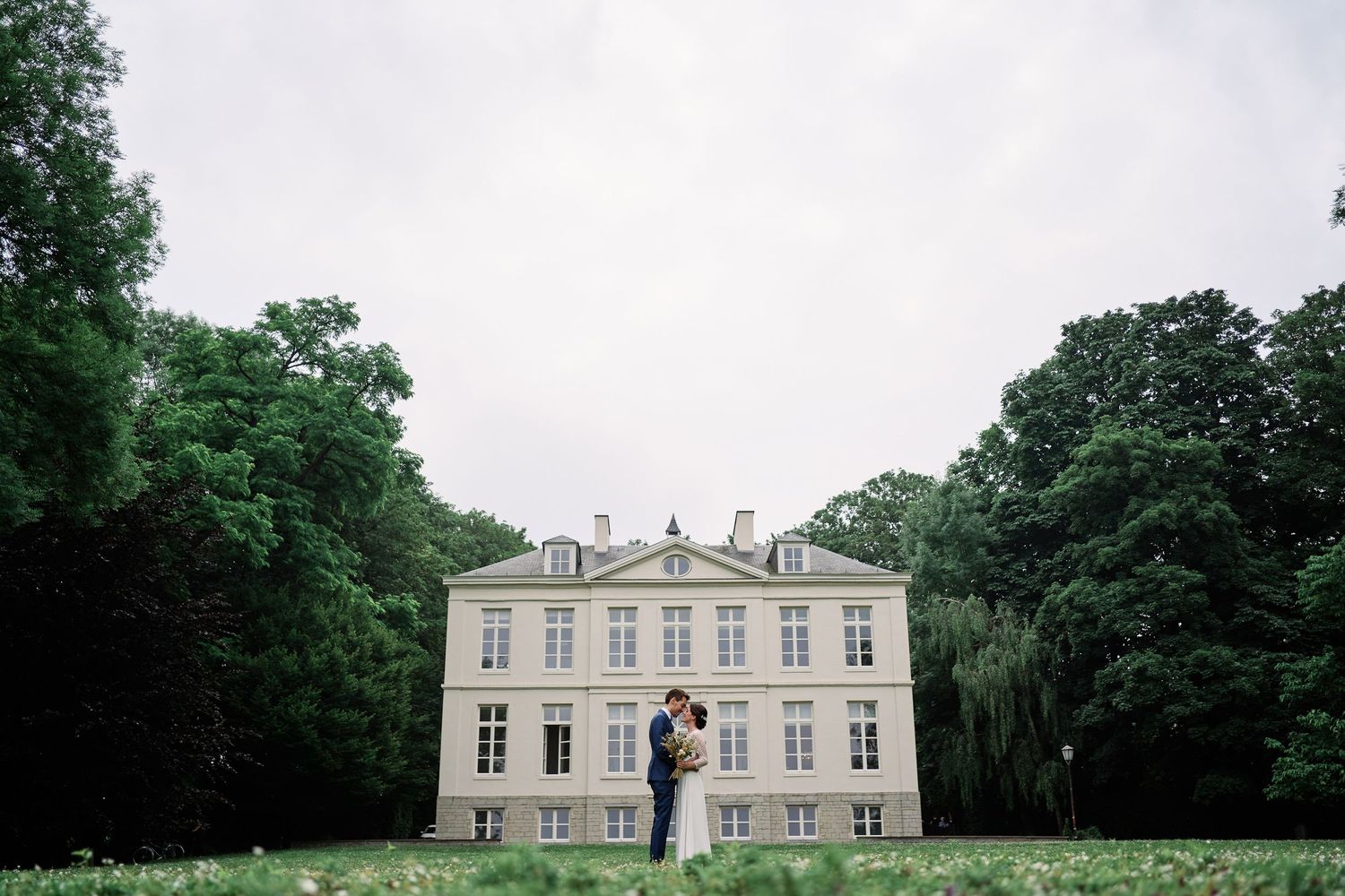 A panoramic view of a grand historic manor house with white facade and classical architecture set among green gardens.