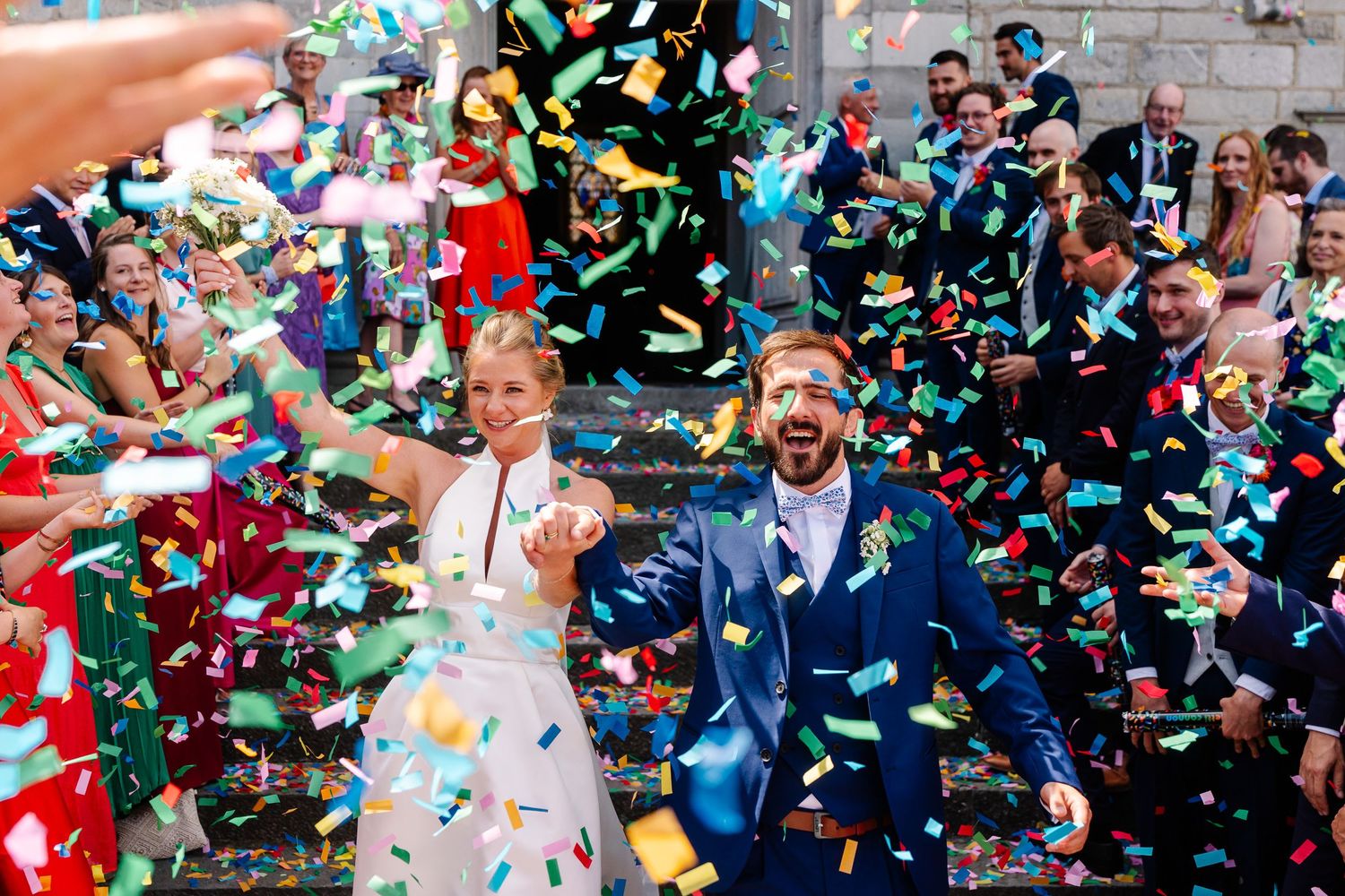 Wedding guests shower newlyweds with colorful confetti during outdoor celebration.