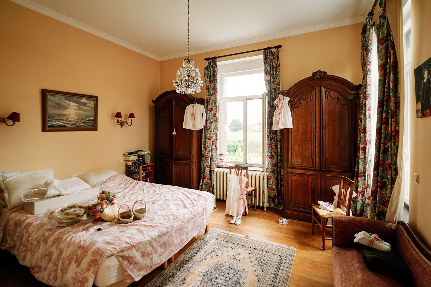 Elegant master bedroom with peach walls features antique wooden furniture, floral curtains, and plush bedding in a panoramic view.