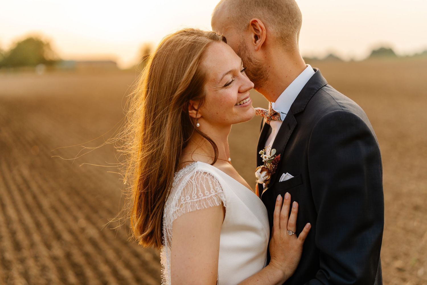 Romantic couple shares intimate moments at sunset in a golden field during their wedding photoshoot.