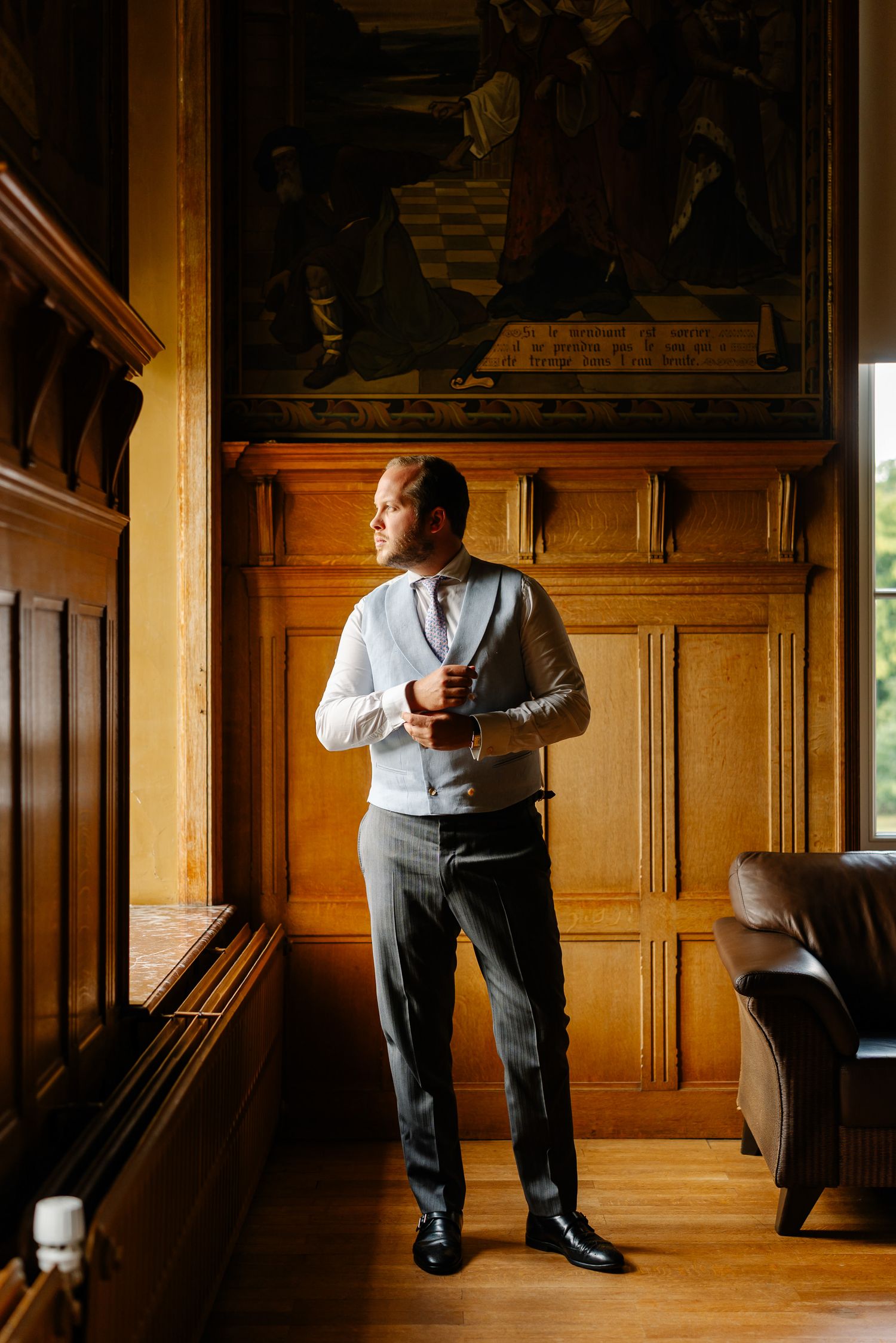 A person wearing a grey vest stands in a wood-paneled room with dramatic lighting and shadows.