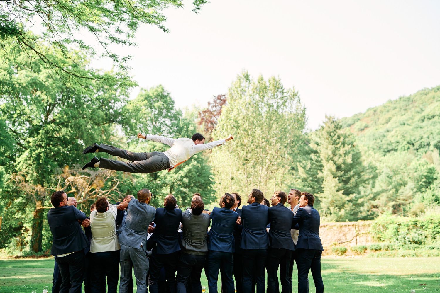 A group of people in formal attire standing together in a garden setting with arms raised in celebration.