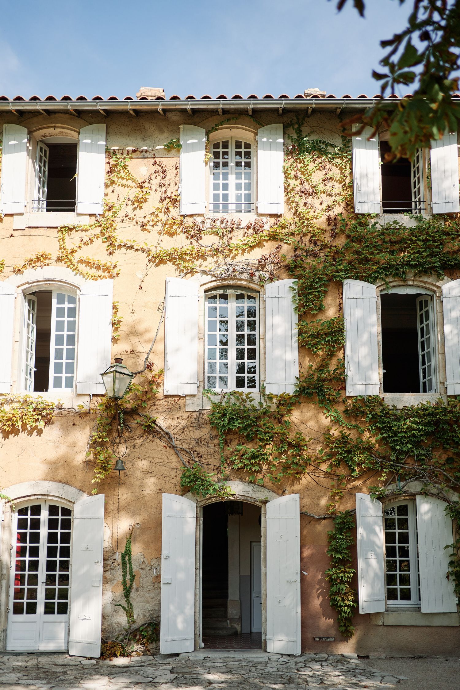 Charming French provincial house with white shuttered windows and climbing vines on a peachy-colored facade in Provence.