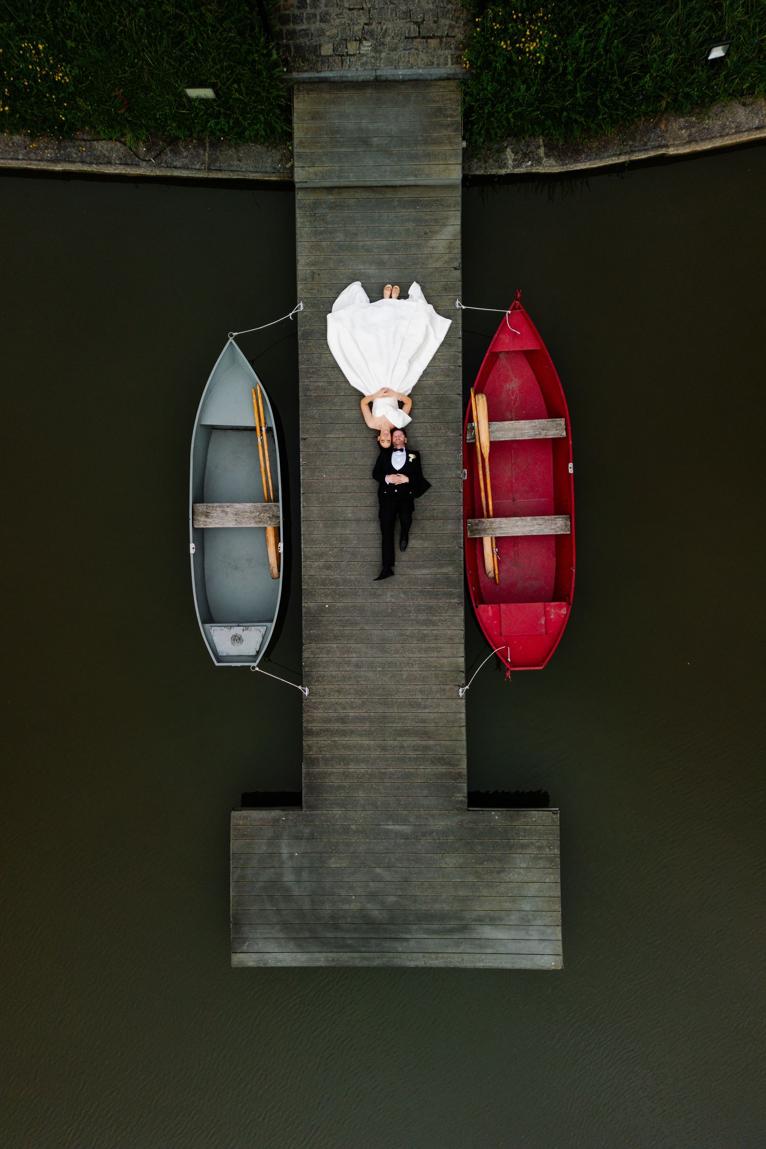 Aerial view of two boats docked at a wooden pier on dark water creating a symmetrical composition.