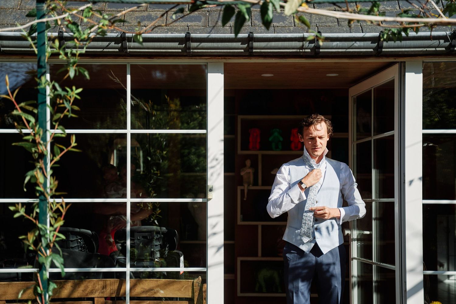 Person wearing a blue shirt stands in front of a window with green plants visible outside.