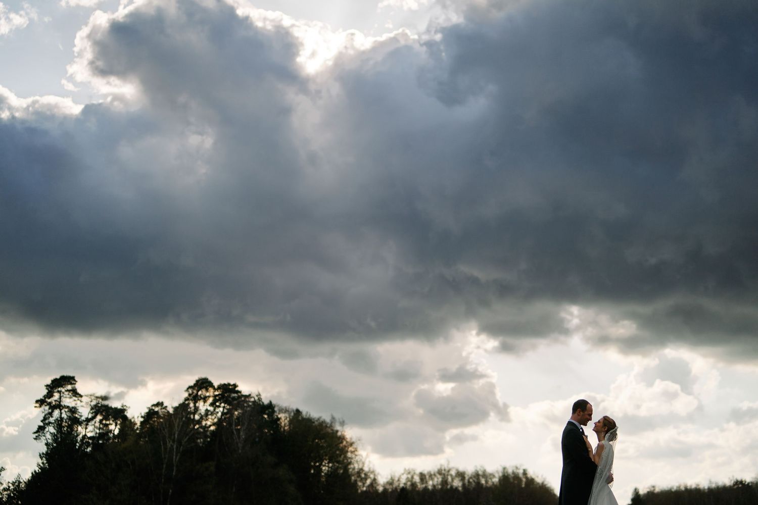 Dramatic silhouettes against a stormy sky with dark clouds and sunbeams breaking through at sunset.