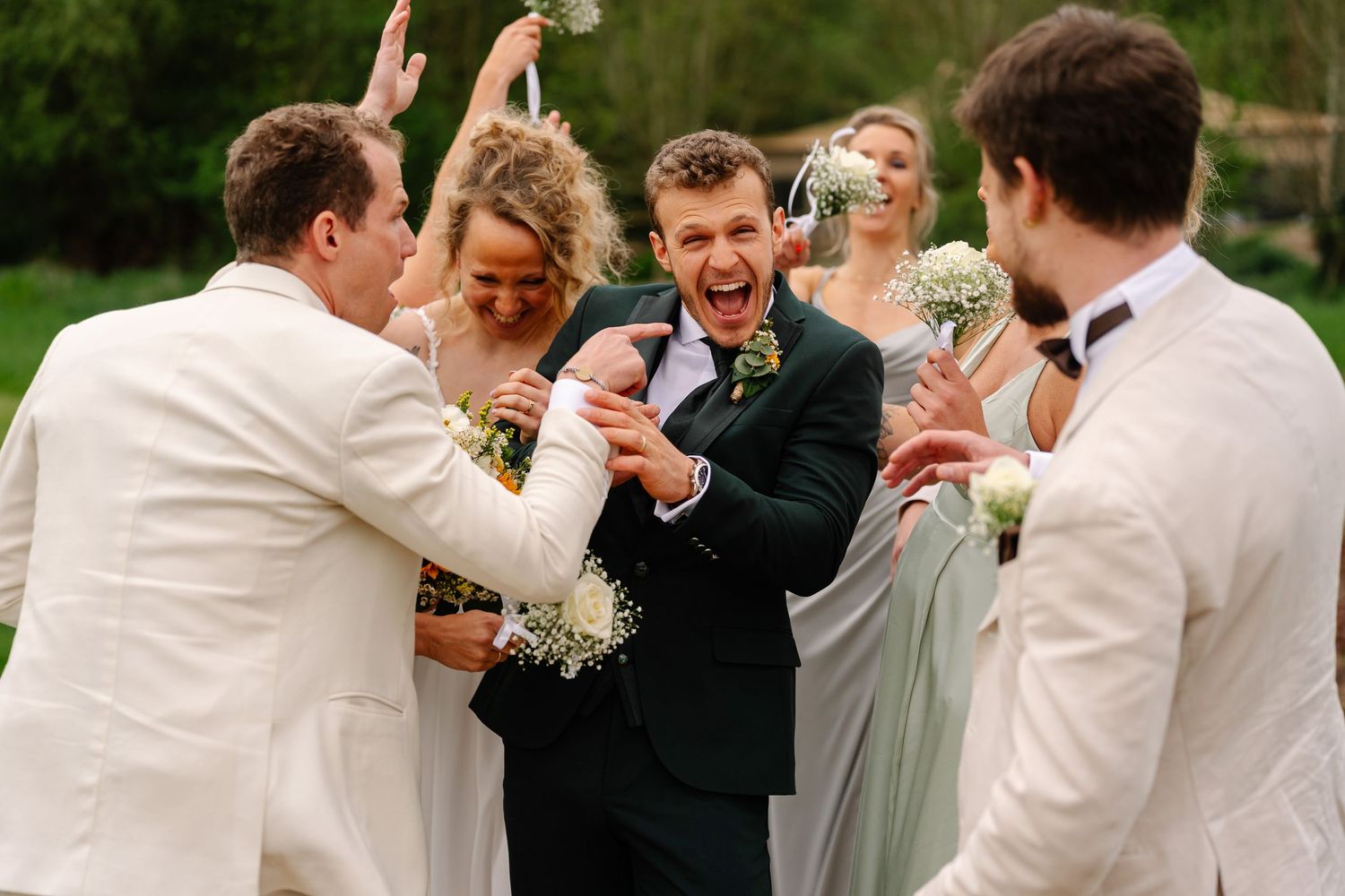 Wedding party members share joyful embraces and greetings during an outdoor celebration.
