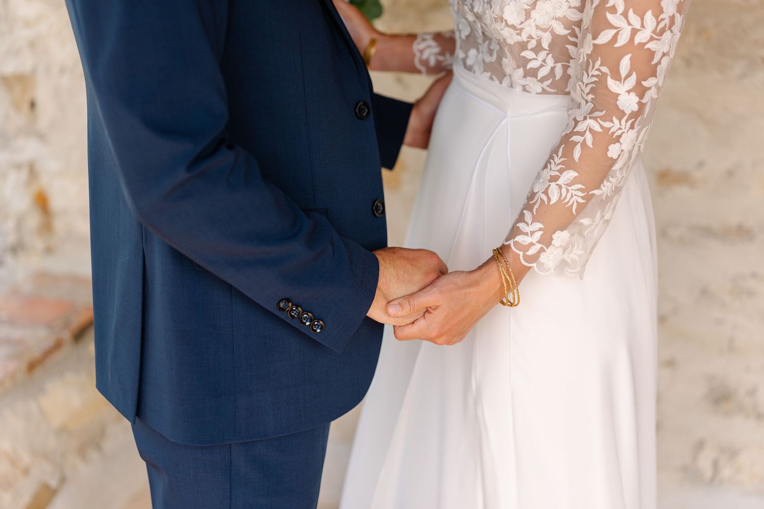 A bride and groom share an intimate moment during their wedding ceremony against a rustic stone wall backdrop.
